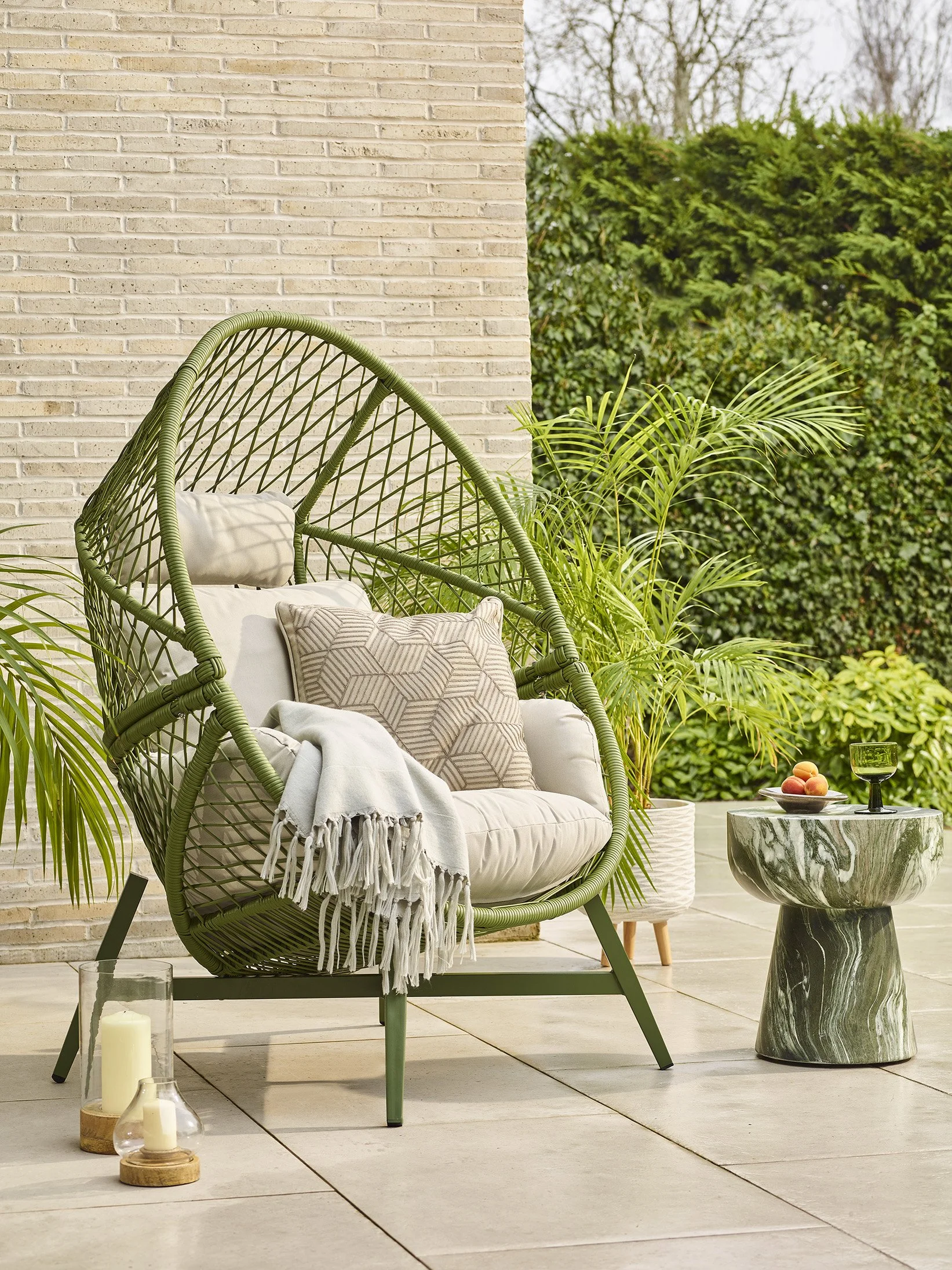 a  freestanding cocoon chair, beige cushions and an outdoor side table in green with a marble effect .