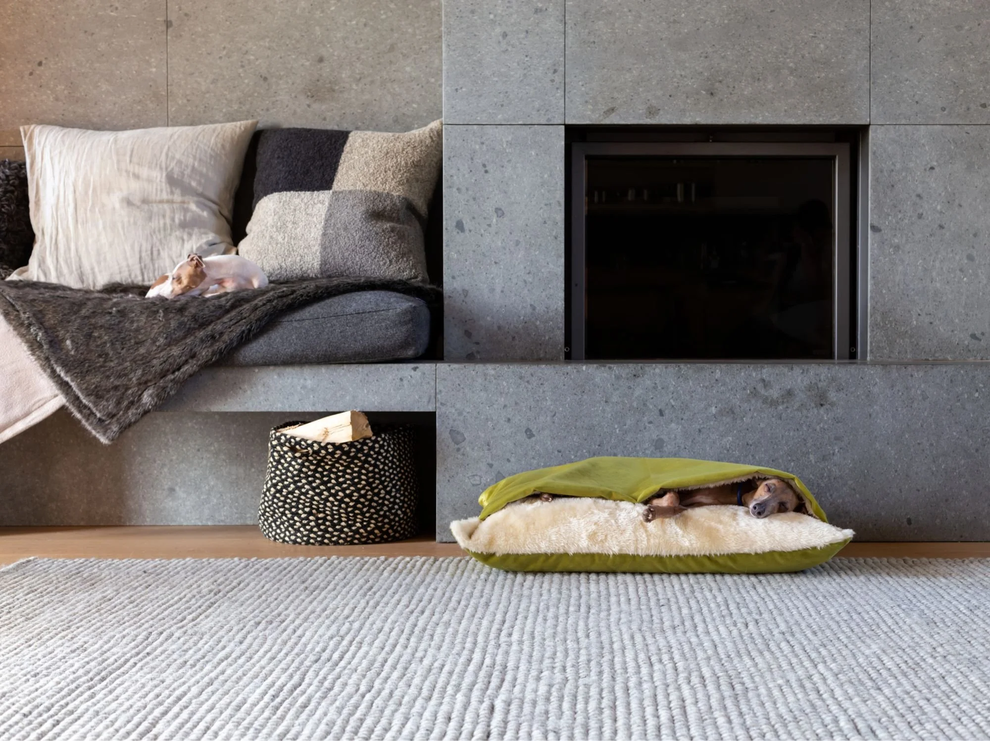 Green dog snuggle bed with soft fleece lining beside a stone fireplace.