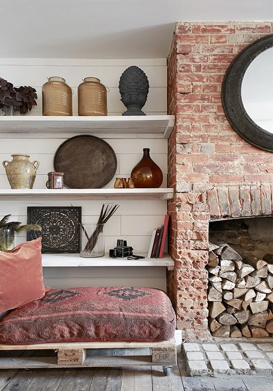A brick fireplace next to white shelves on a shiplap wall with various vases and decorative pieces