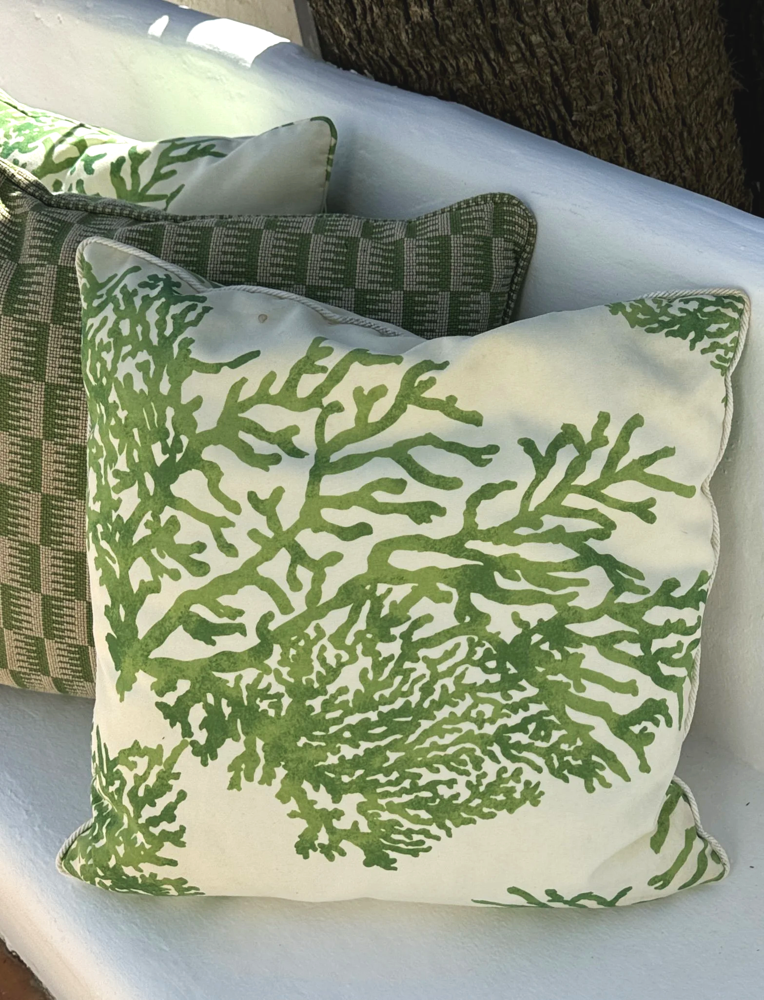 Three cushions on a white plaster bench. Two of the cushions are cream with a bold green print of coral while the middle one has a geometric pattern and is green and beige