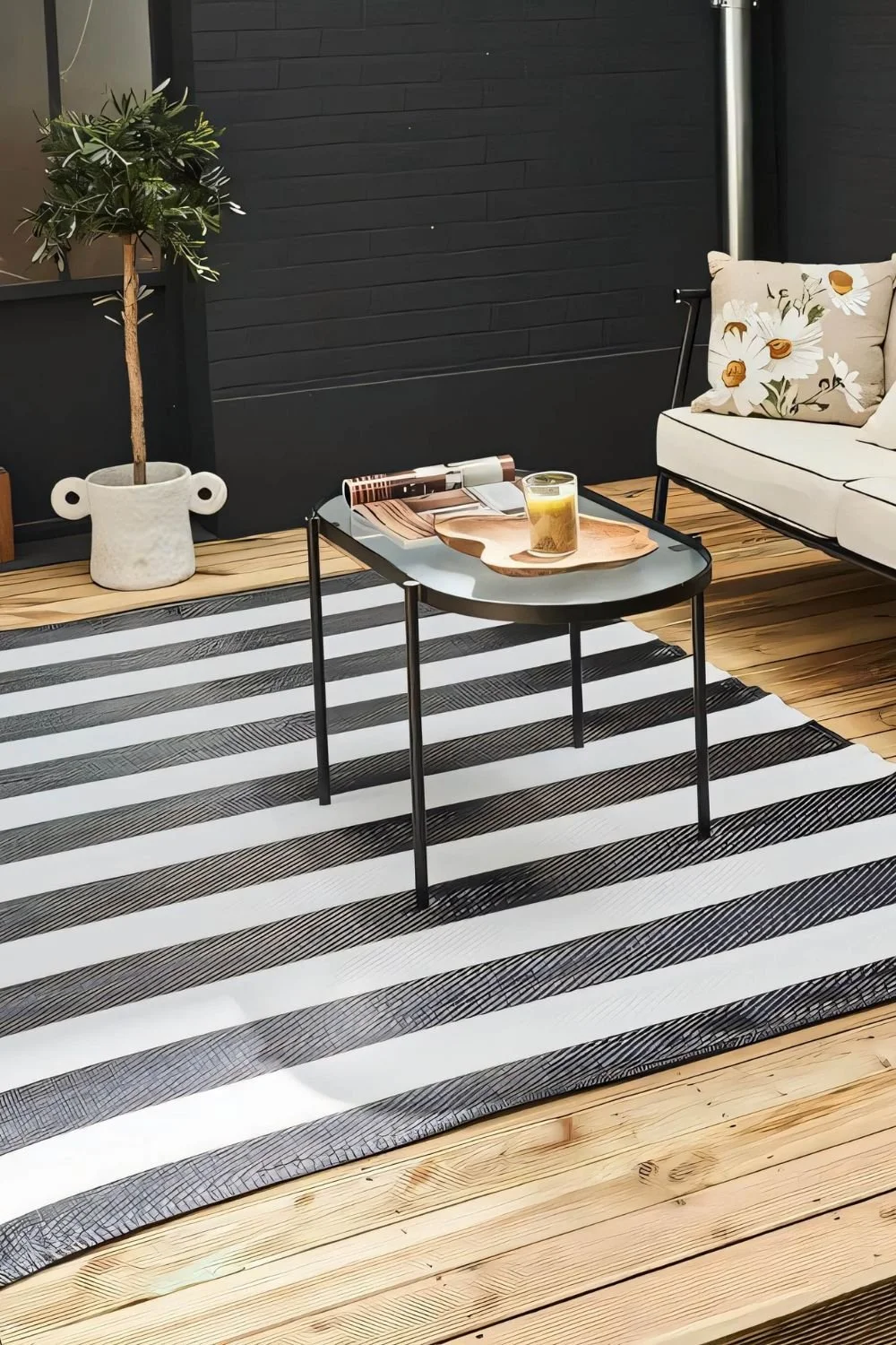 A black and white striped outdoor rug with a black steel coffee table and black sofa with white cushions