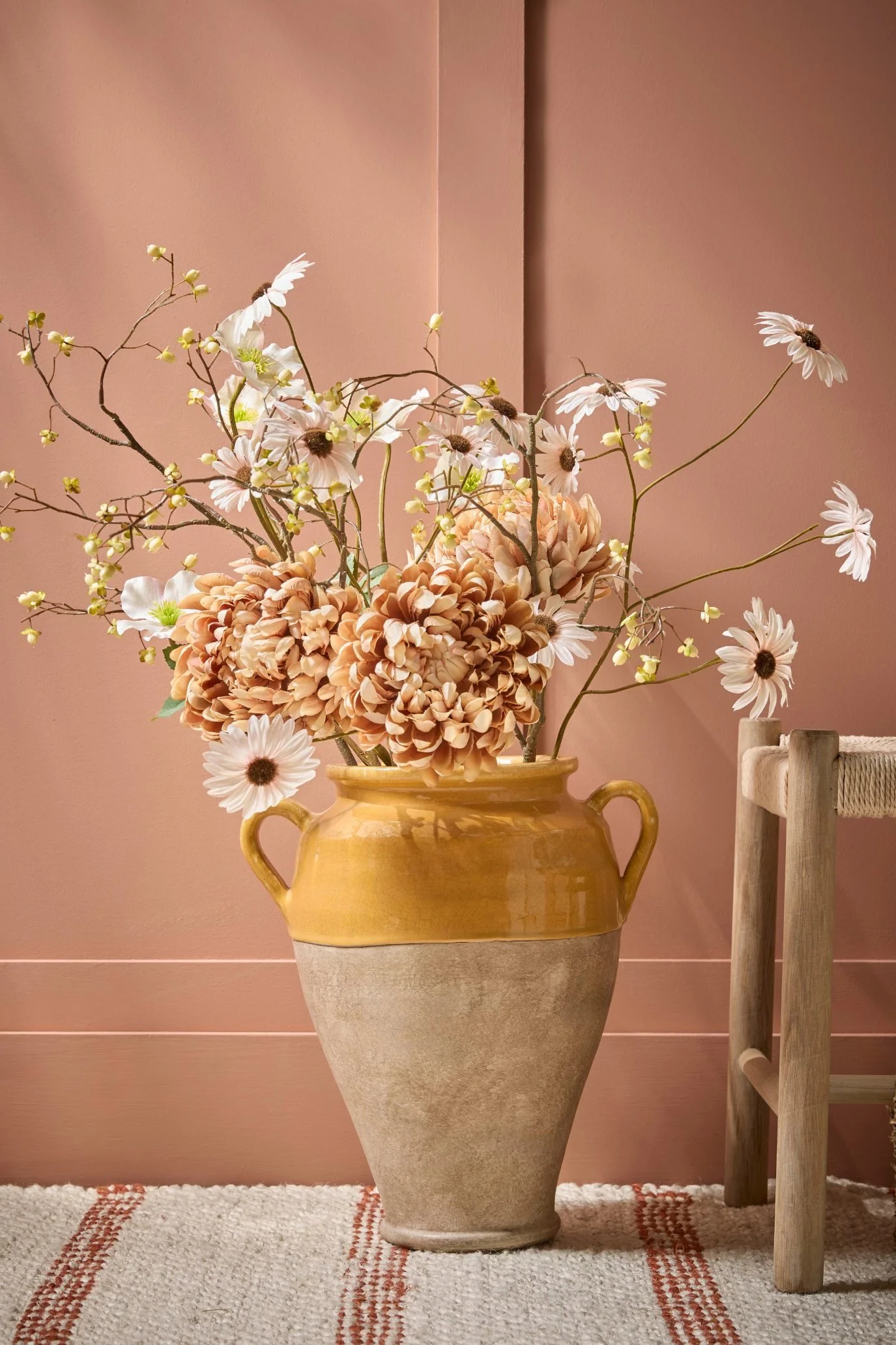 Peach and white faux flowers arranged in an ochre glazed stoneware vase.