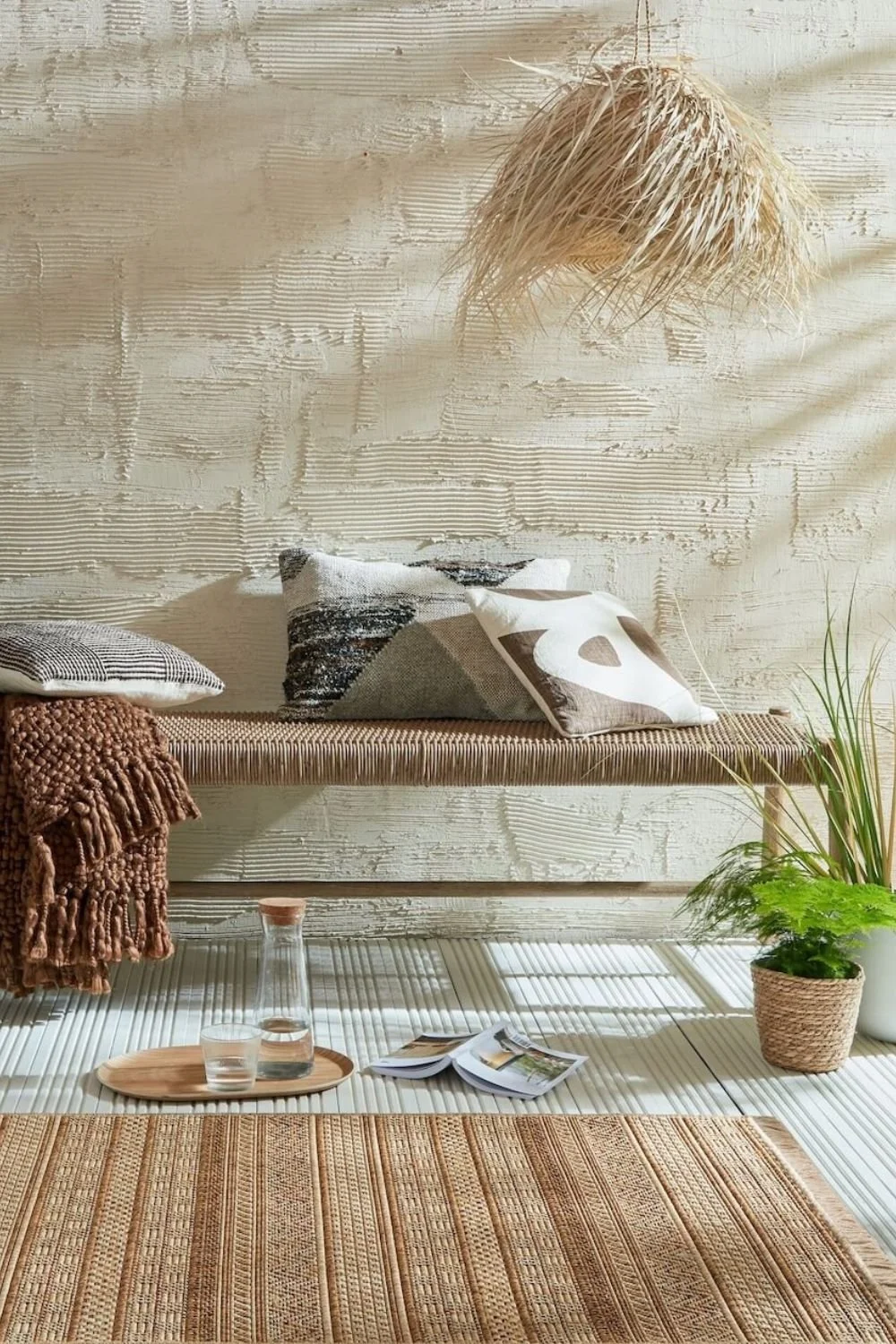 A neutral woven outdoor striped rug next to a beige stool and raffia pendant