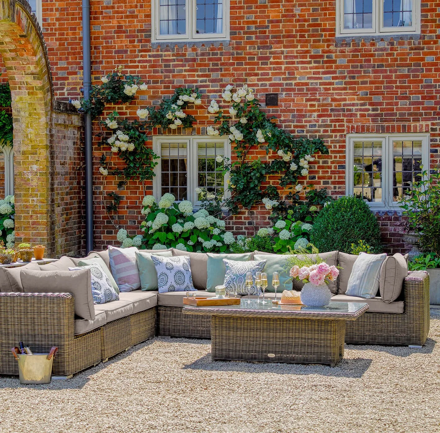 Country garden patio with a woven outdoor sofa and layered blue and neutral cushions