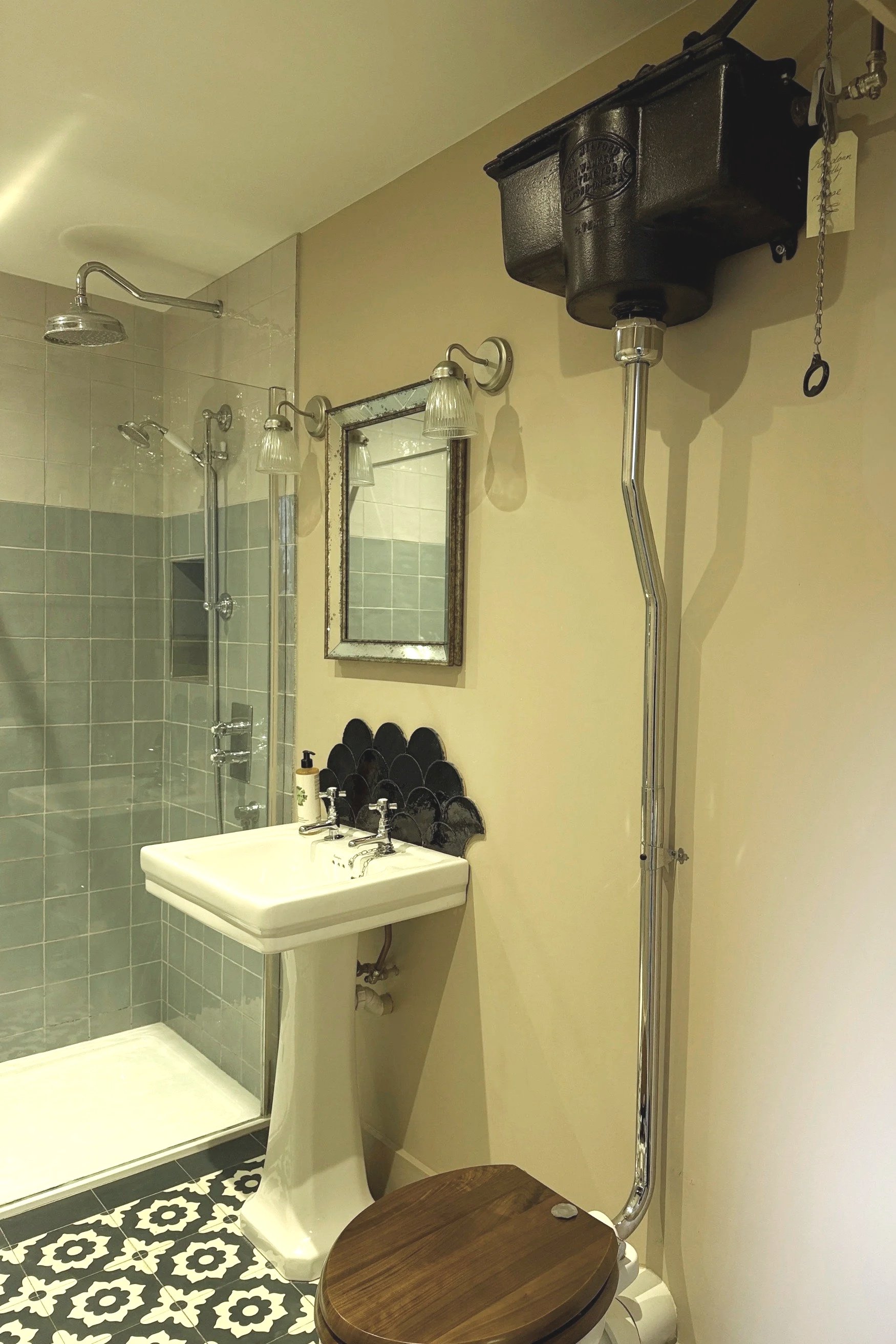 A bathroom with an old high-level toilet cistern, a traditional pedal stool basin, and a shower enclosure with pale green tiles