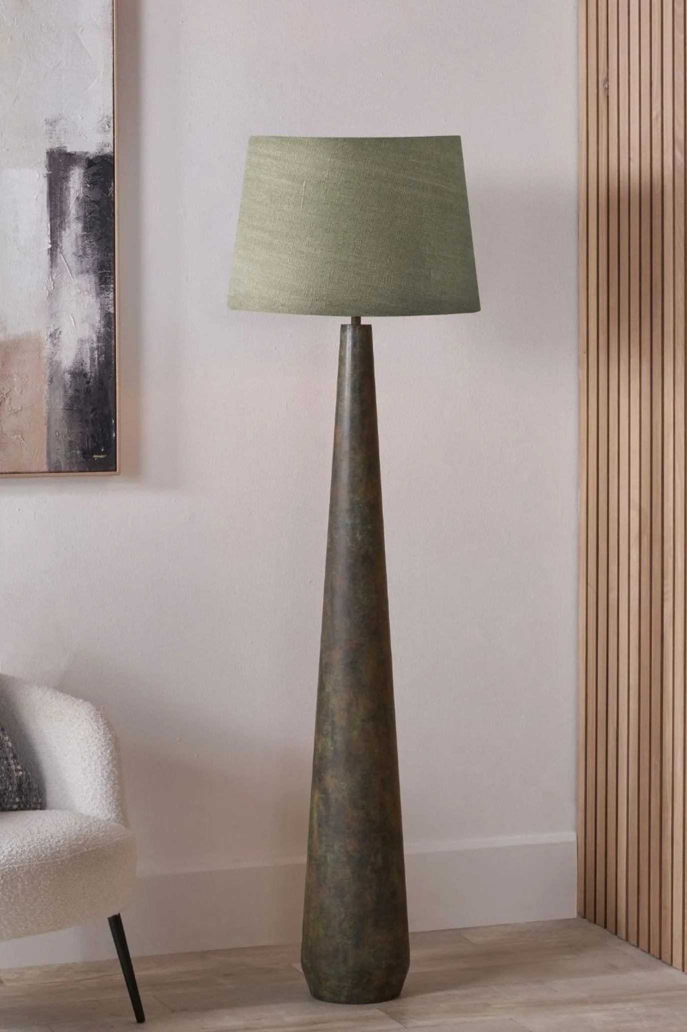 Tall tapered floor lamp with an aged brown-green base and sage green shade beside a cream sofa.