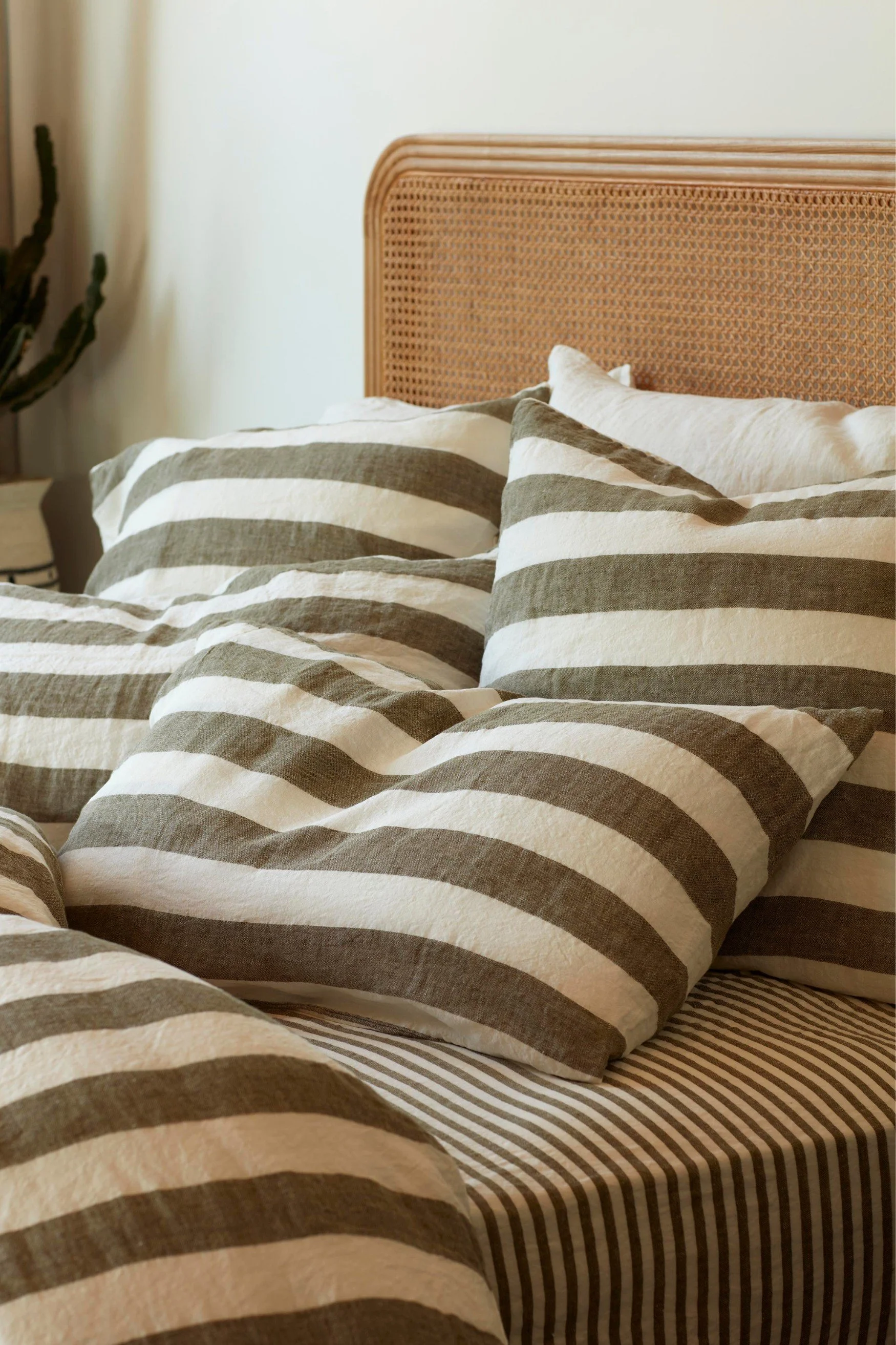 a cane headboard with pillows and a duvet cover in large olive green stripes with a sheet underneath in small stripes
