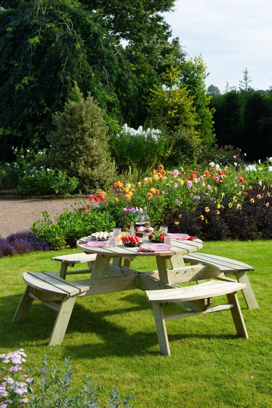 Wooden round picnic table with attached benches styled for outdoor dining in a colourful cottage garden.