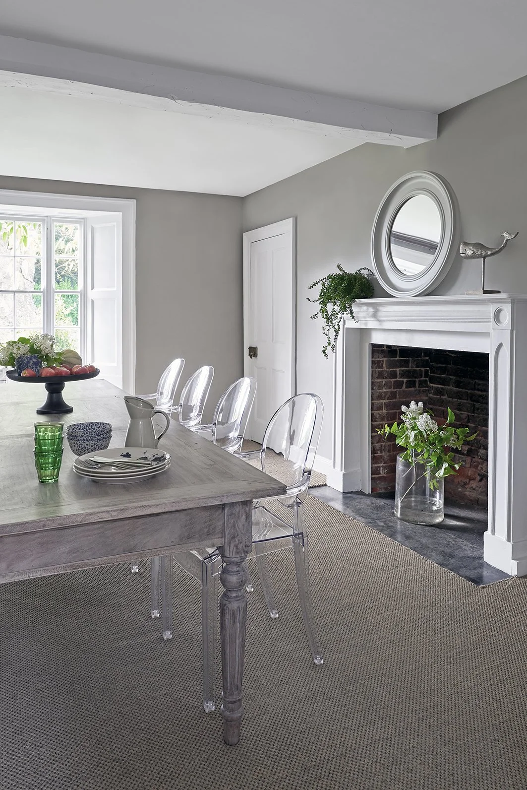 Dining room with table and clear plastic chairs with a fireplace and a large vase of flowers in the hearth