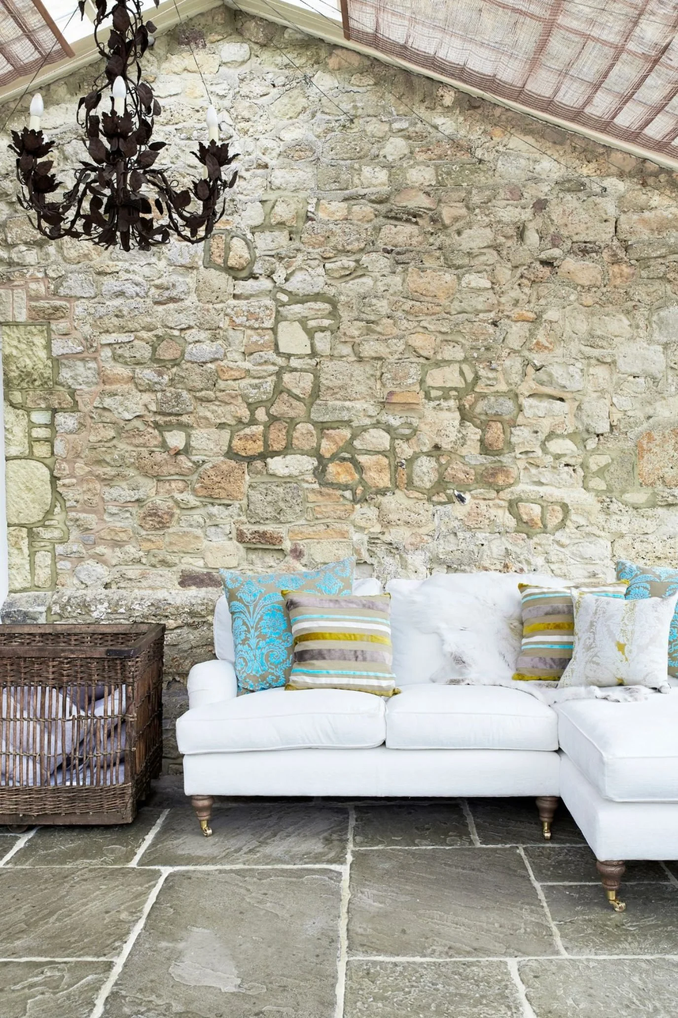Rustic orangery with stone walls, flagstone flooring, white sofa and velvet cushions in aqua and taupe