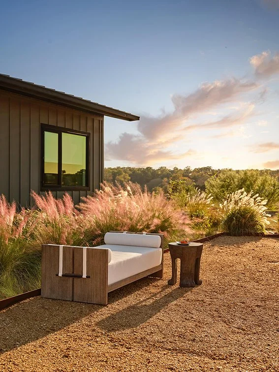 contemporary outdoor daybed in teak with a Crean cushion base on a sandy terrace next to grasses