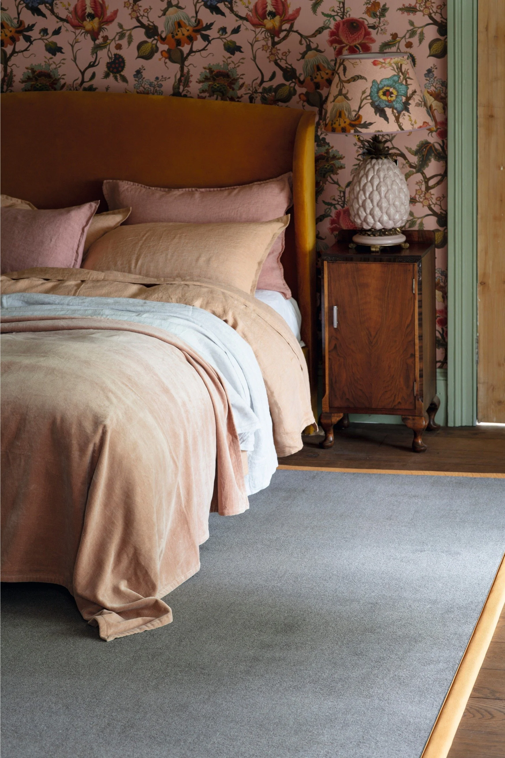 A bedroom with a bed in peachy toned linen on a grey rug with a yellow border