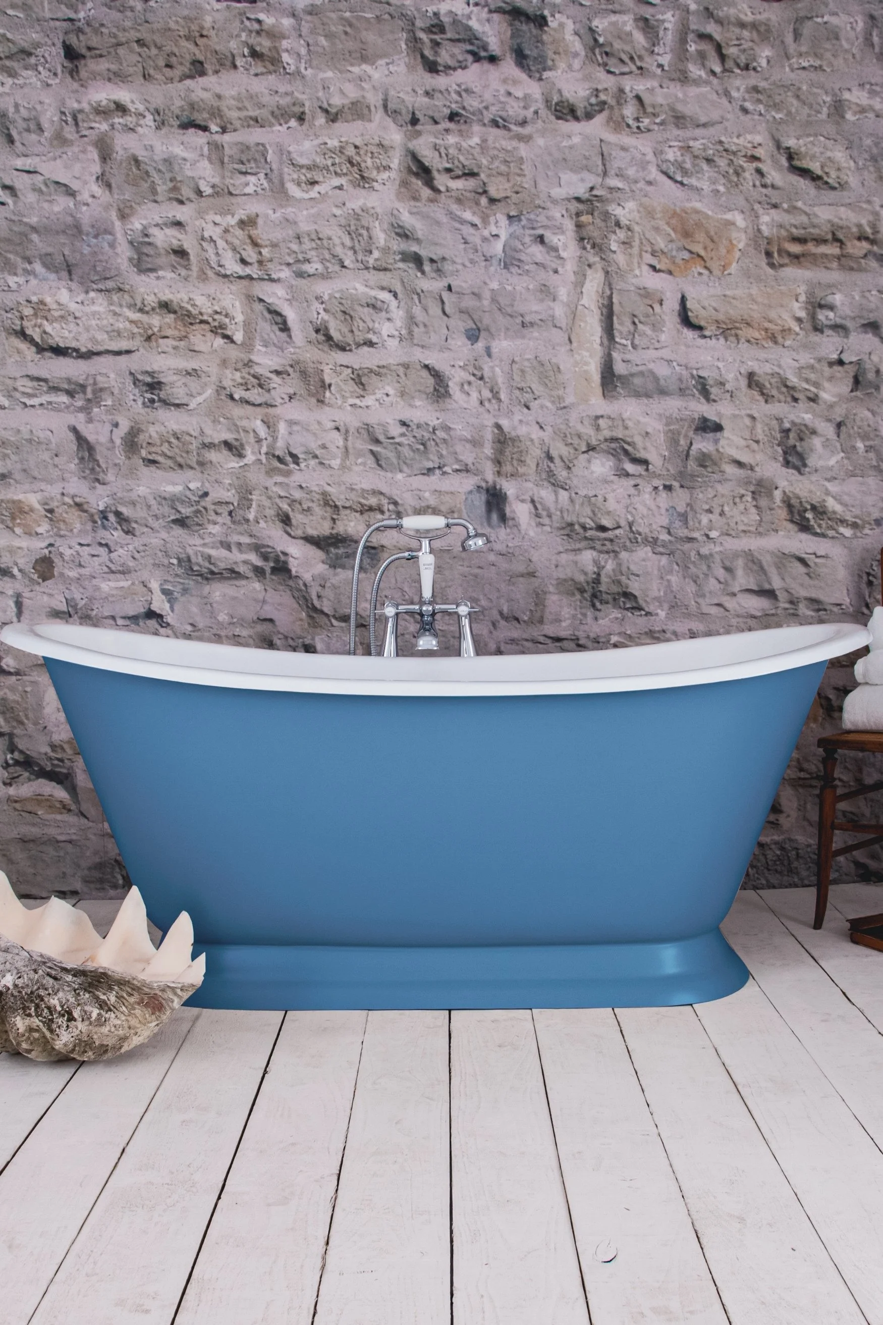A blue rolltop bath on a wooden floor infront of a rough stone wall