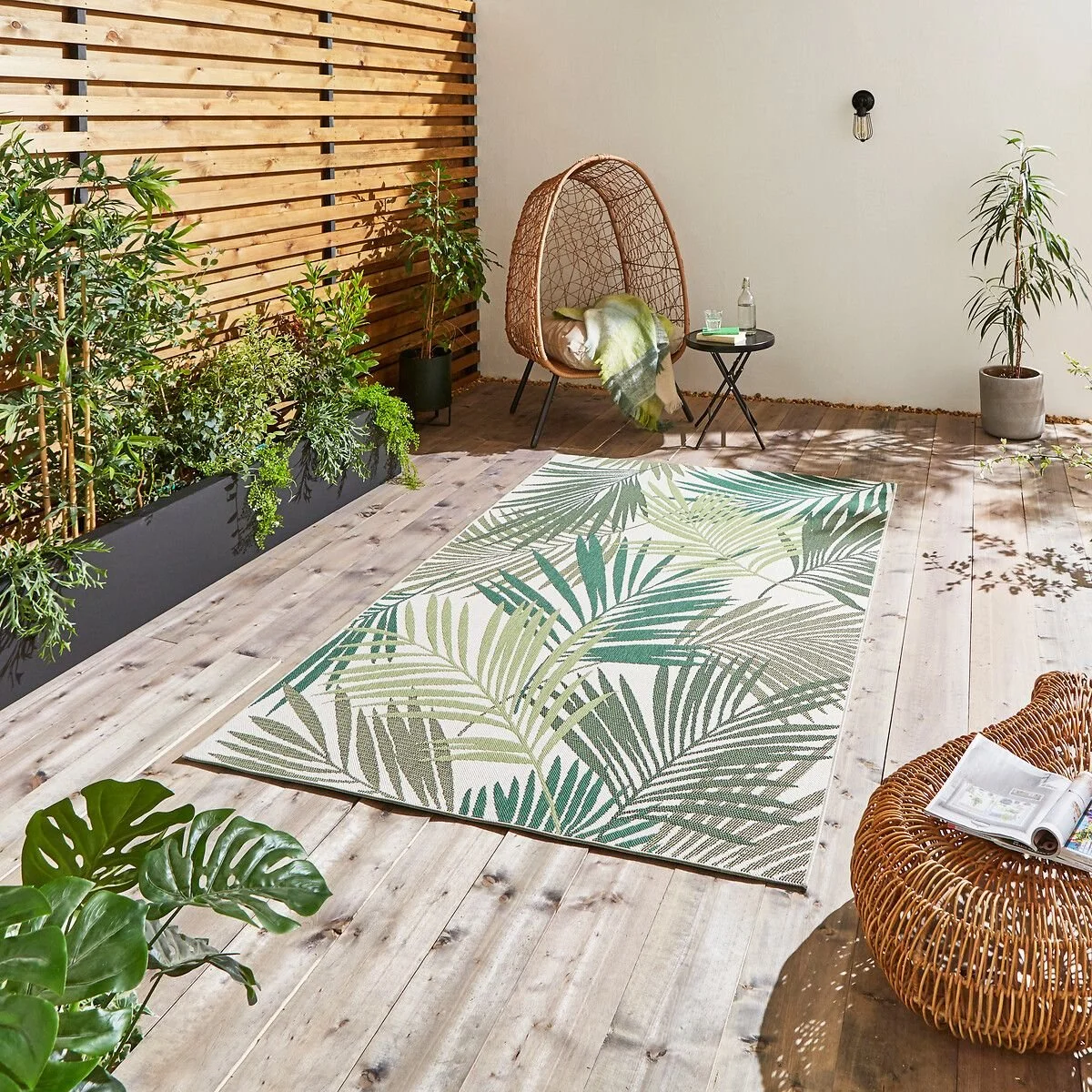 A decking with a tropical rug in green and brown and an egg chair with a small side table in the corner