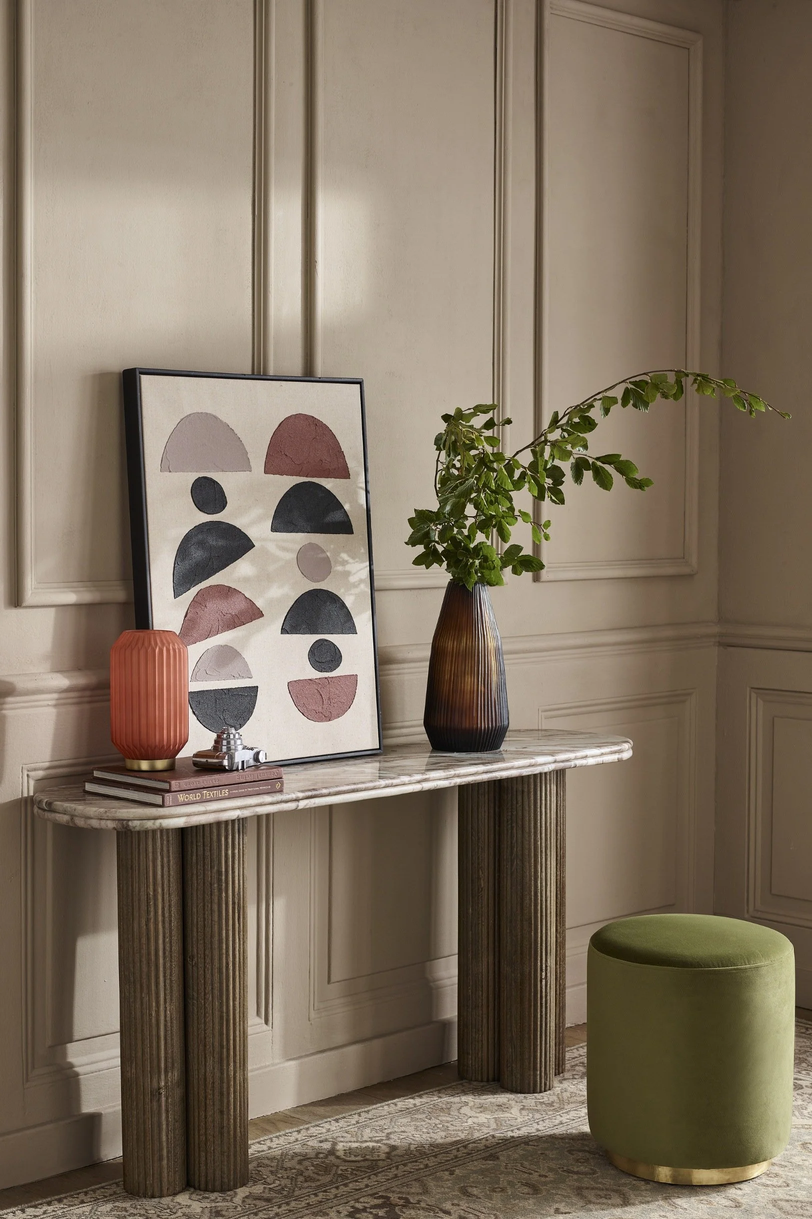 A rounded console table with a large frame and modern art, lamp and vase all displayed on it