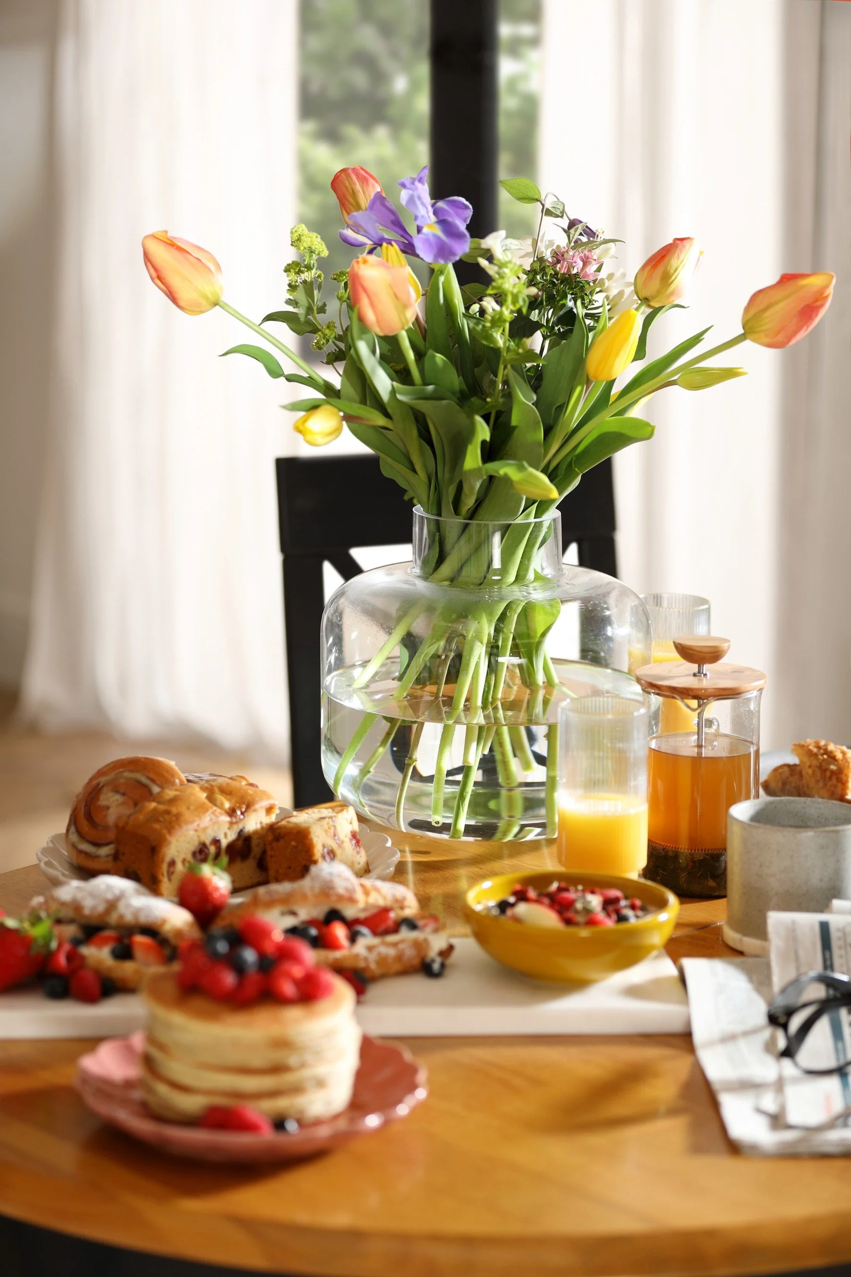 A breakfast table with pancakes, berries and a vase filled with tulips and an iris
