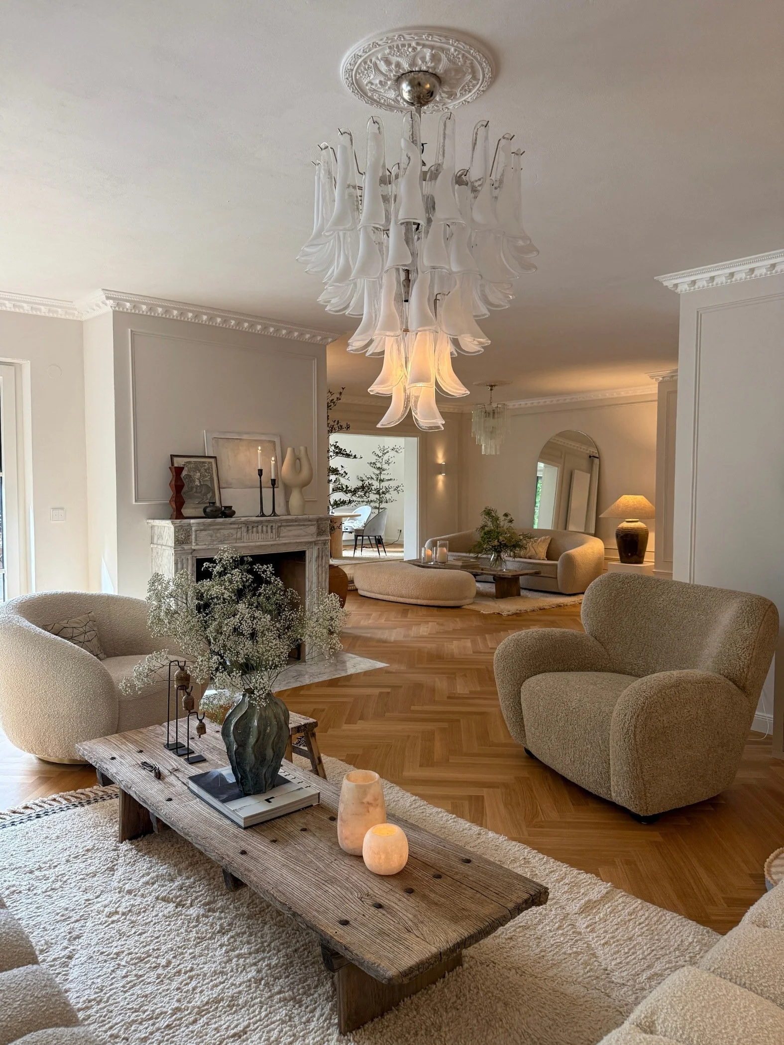 Living room with cream sofas, two boucle chairs, a cream rug and wooden coffee table with a large glass chandelier hanging above