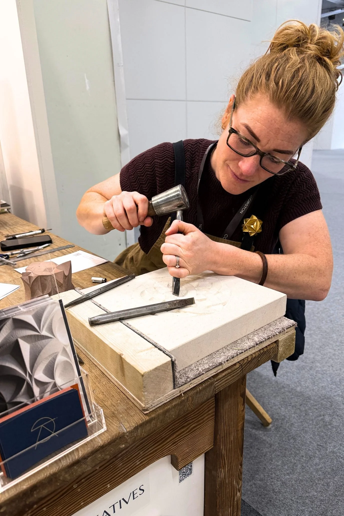 Artisan using a chisel and mallet to carve a decorative panel during a live demonstration at Decorex.
