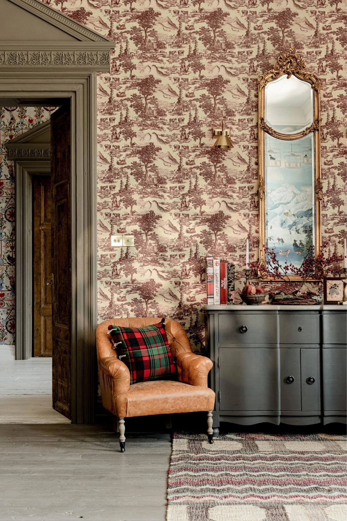 MINDTHEGAP Toile de Jouy wallcovering in deep red with coordinating rug and flowers in a bedroom.