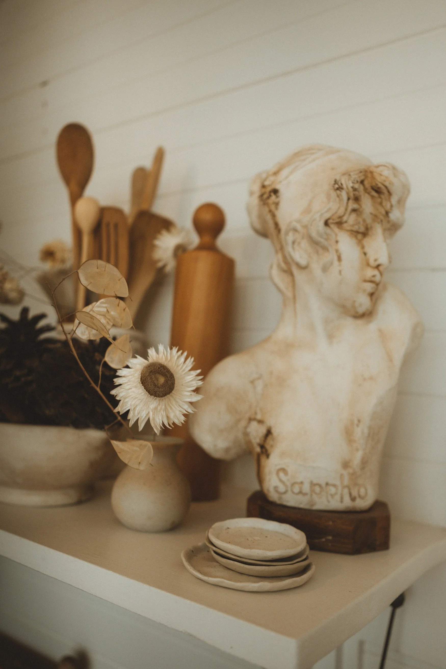 A shelf with a vintage bust, earthen ware dishes and wooden utensils with dried flowers