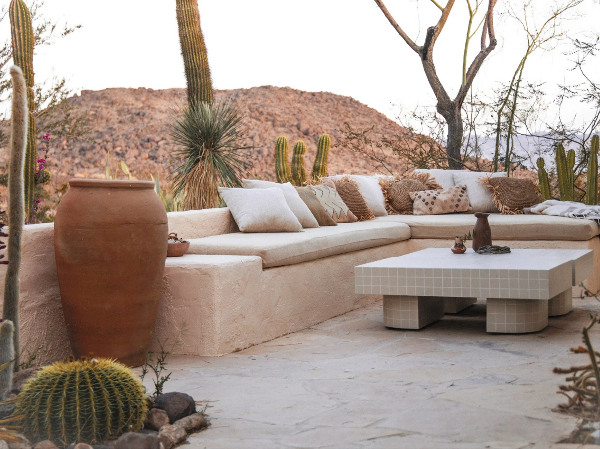 Outdoor terrace at The Joshua Tree House with layered cushions, rustic furniture and panoramic desert views.