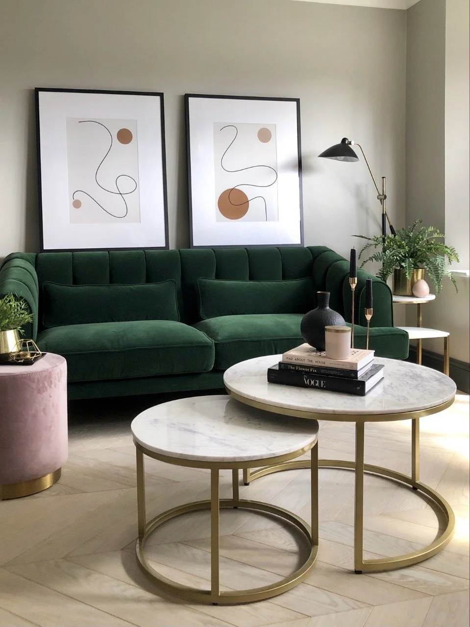 A green sofa with two nesting tables with books, vases and candle holders on top. Two large framed artwork are leaning against the sofa