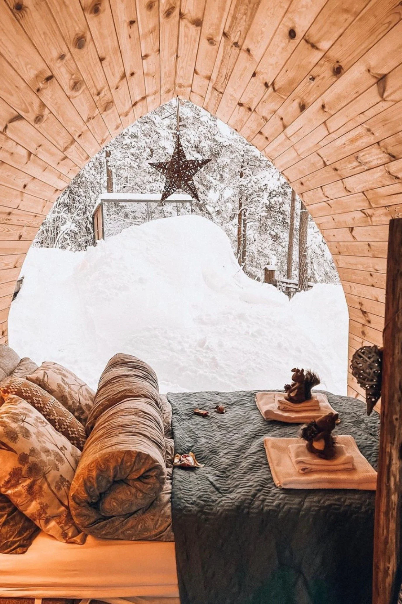 Outdoor sleeping cabin at WonderInn surrounded by snow-covered forest with cosy bedding and nature views.