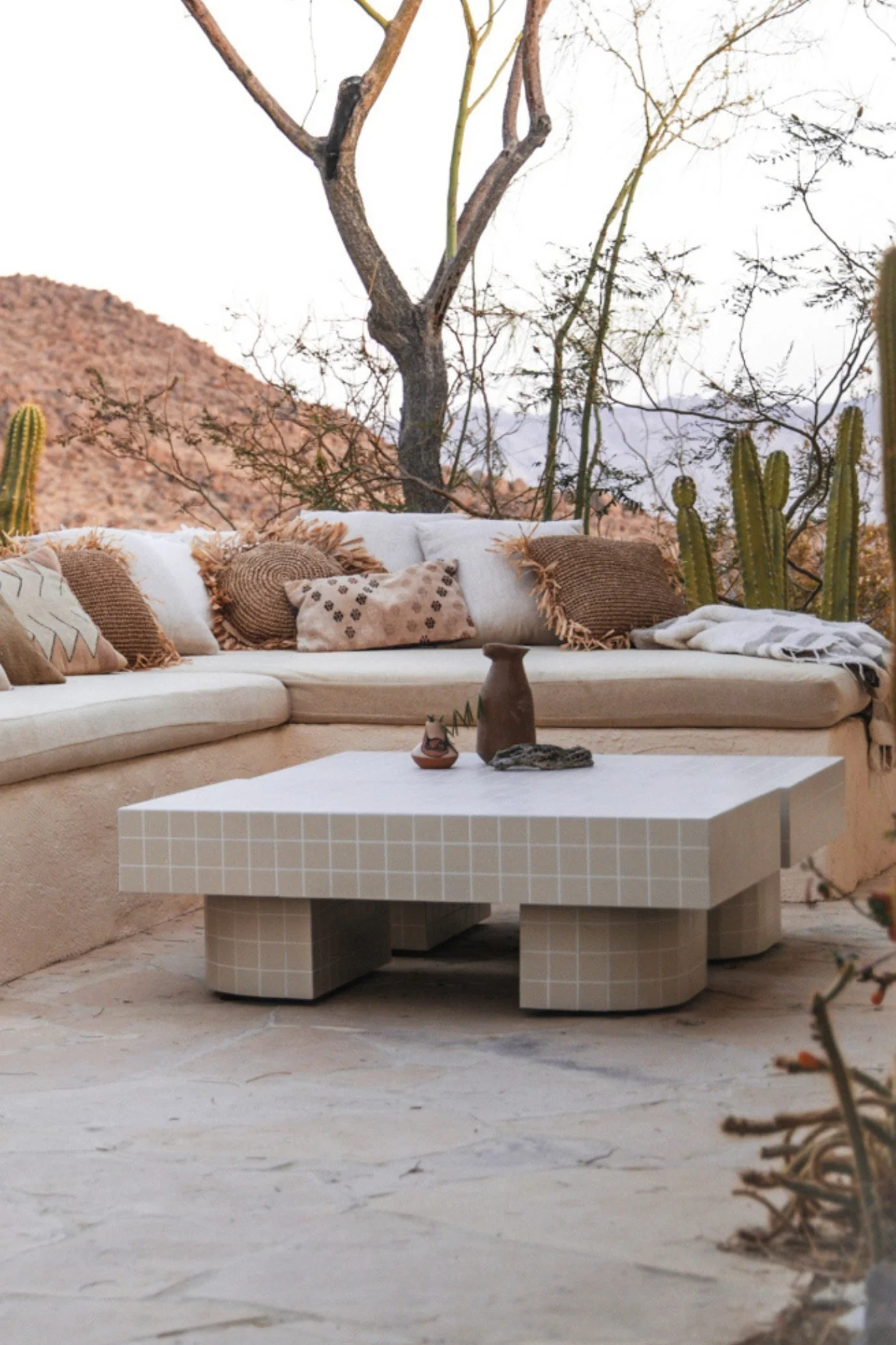 An outdoor terrace with plaster benches styled with a mixture of cushions in the desert