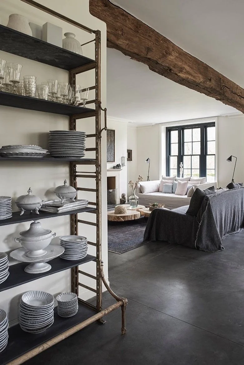Vintage shelving with tableware looking through to a seating area with a dark grey sofa and a lighter toned sofa under a large wooden beam