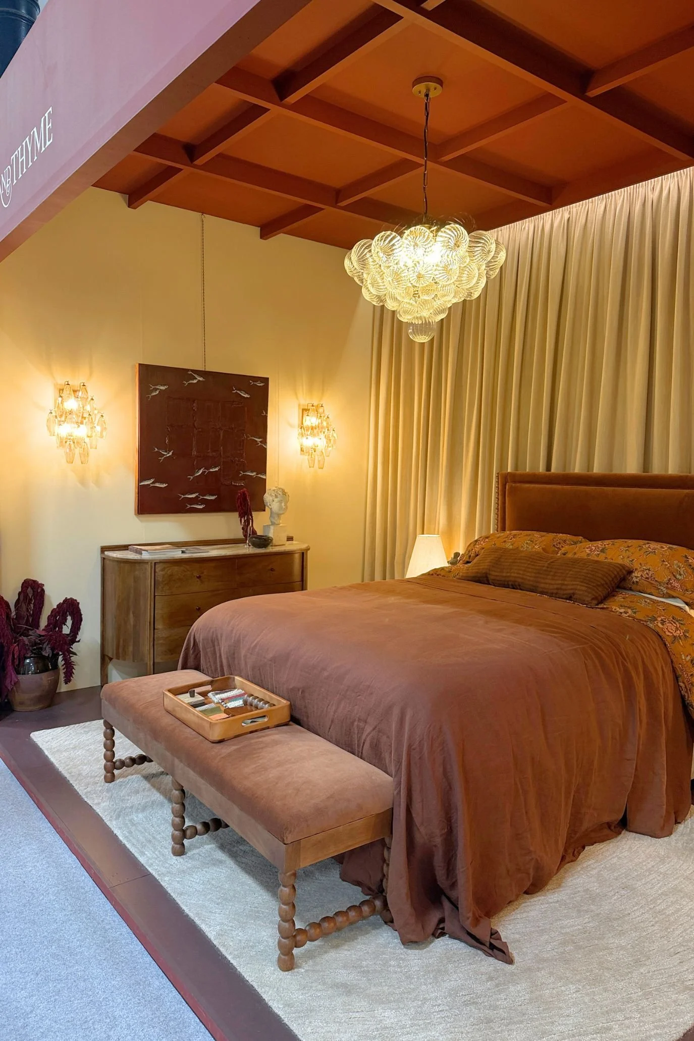 Bedroom display on the Atkin and Thyme stand, with a timber ceiling, pendant light and full-length curtains.