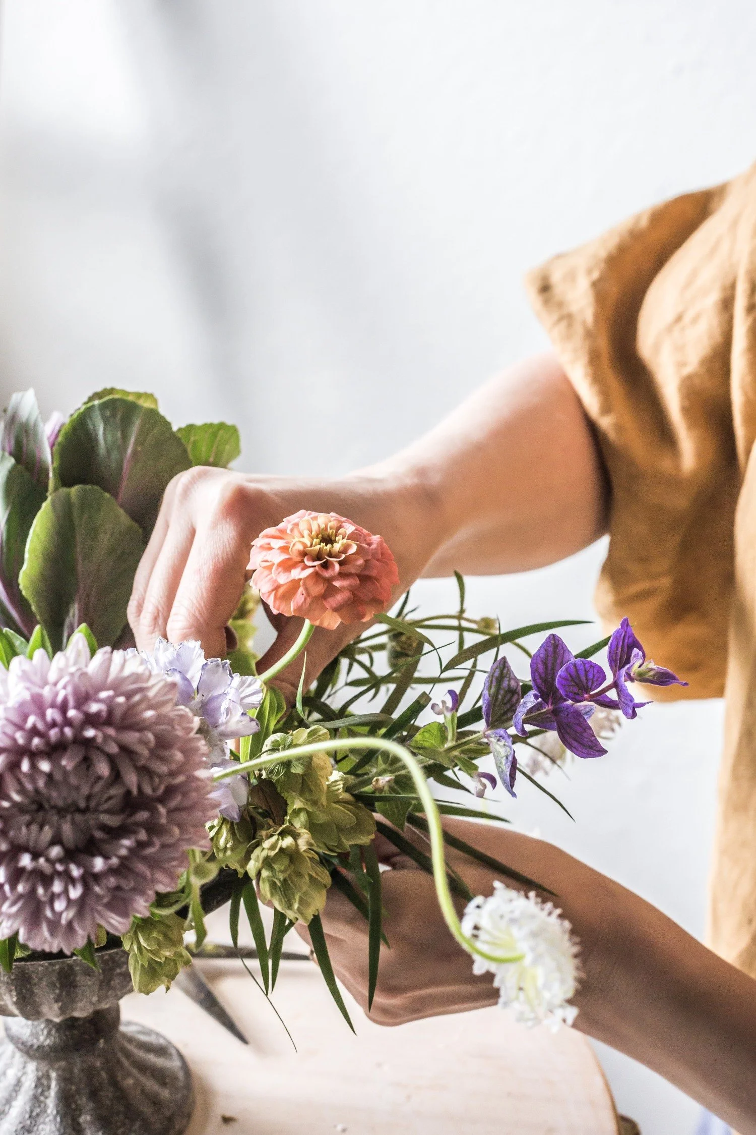 A woman's arm and hand placing a peach toned flower into a floral arrangement