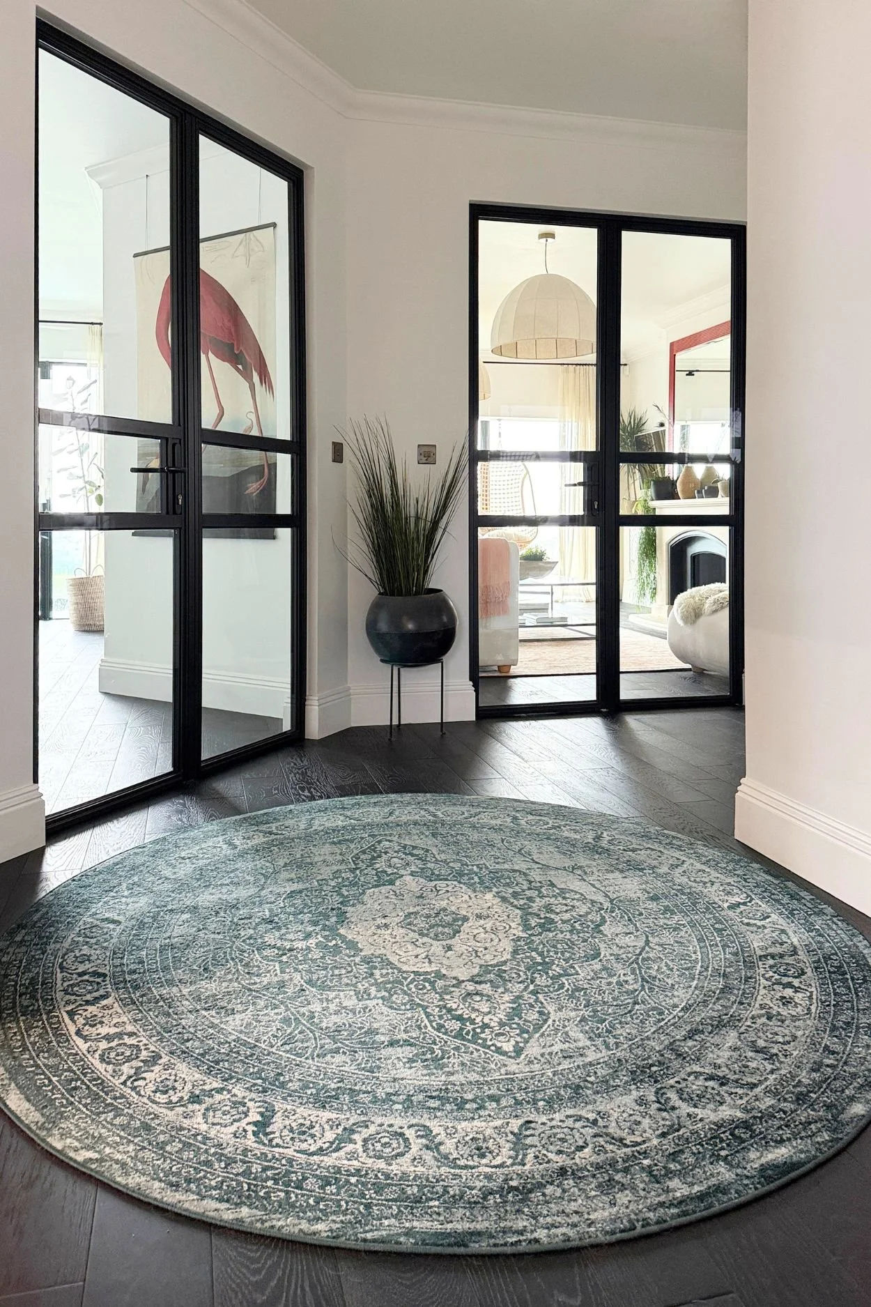 a circular patterned vintage style rug next to a green leather sofa with a green cushion and house plant in pot with feet on the floor.