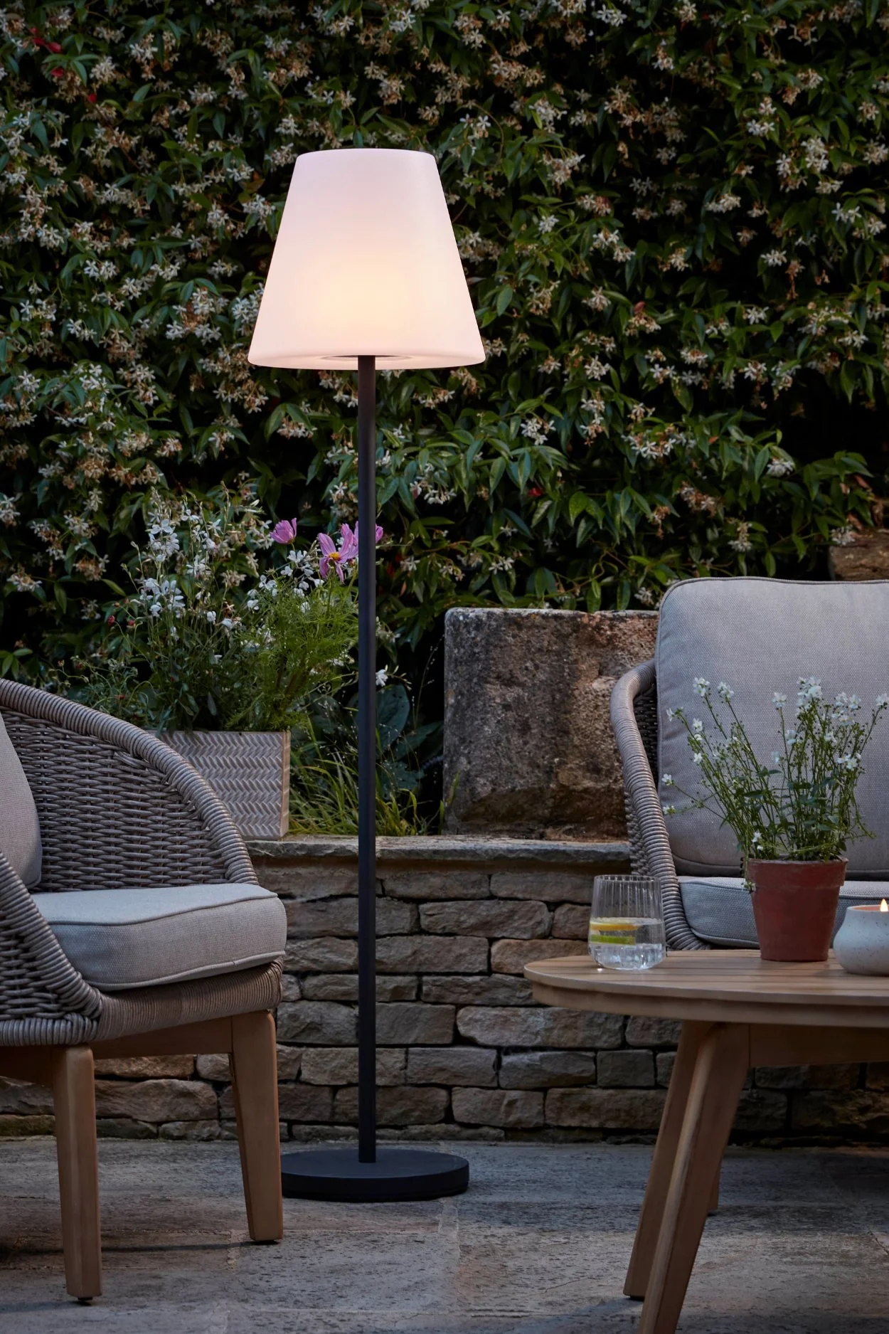 Portable outdoor floor lamp styling a comfortable garden seating area for relaxing after dark.