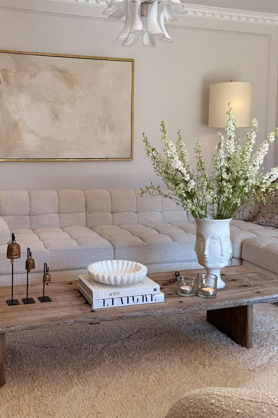 a coffee table with three vintage bells, two books, a white dish and large white vase with faces on and white flowers