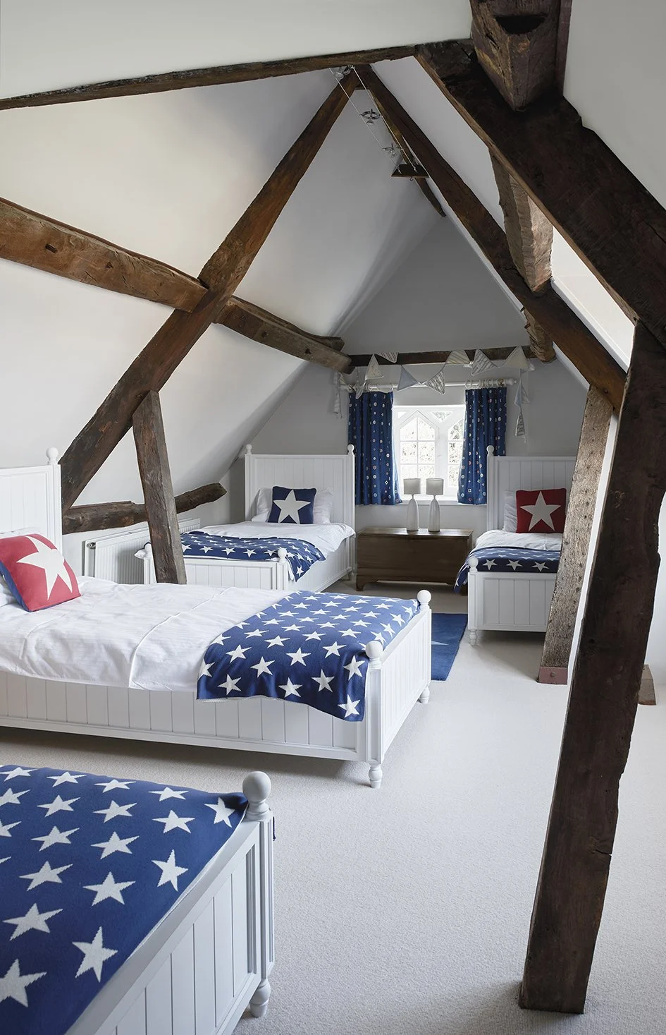 An attic bedroom with wooden beams and four beds with stars on cushions and throws