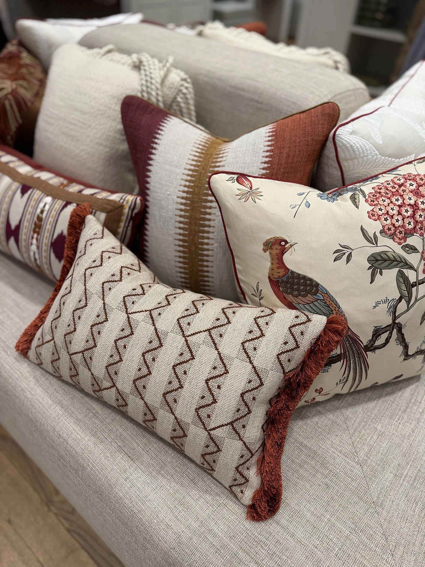 a mixture of cushions  with different shapes and trims in earthy colours including the design of a peacock on a cushion