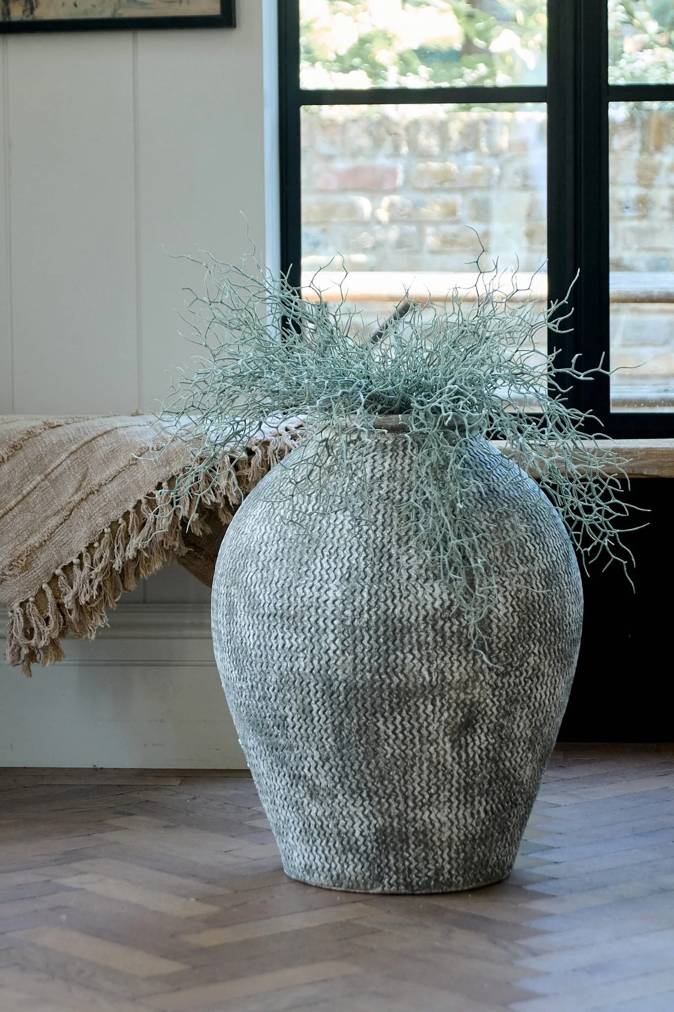 Large textured floor vase styled with decorative branches in a modern living room.