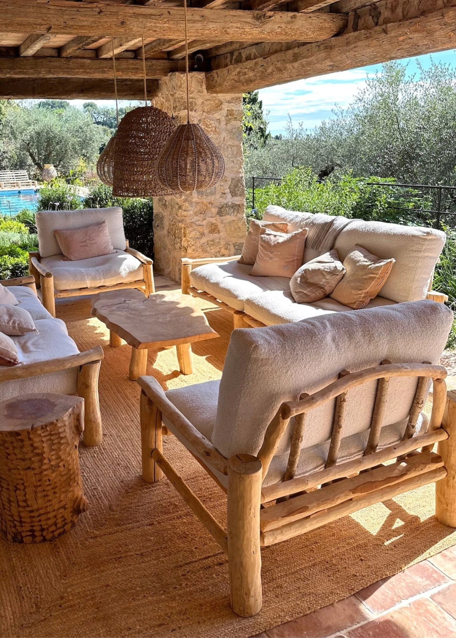 A terrace infront of a pool with rattan pendants and sofas and chairs made from driftwood