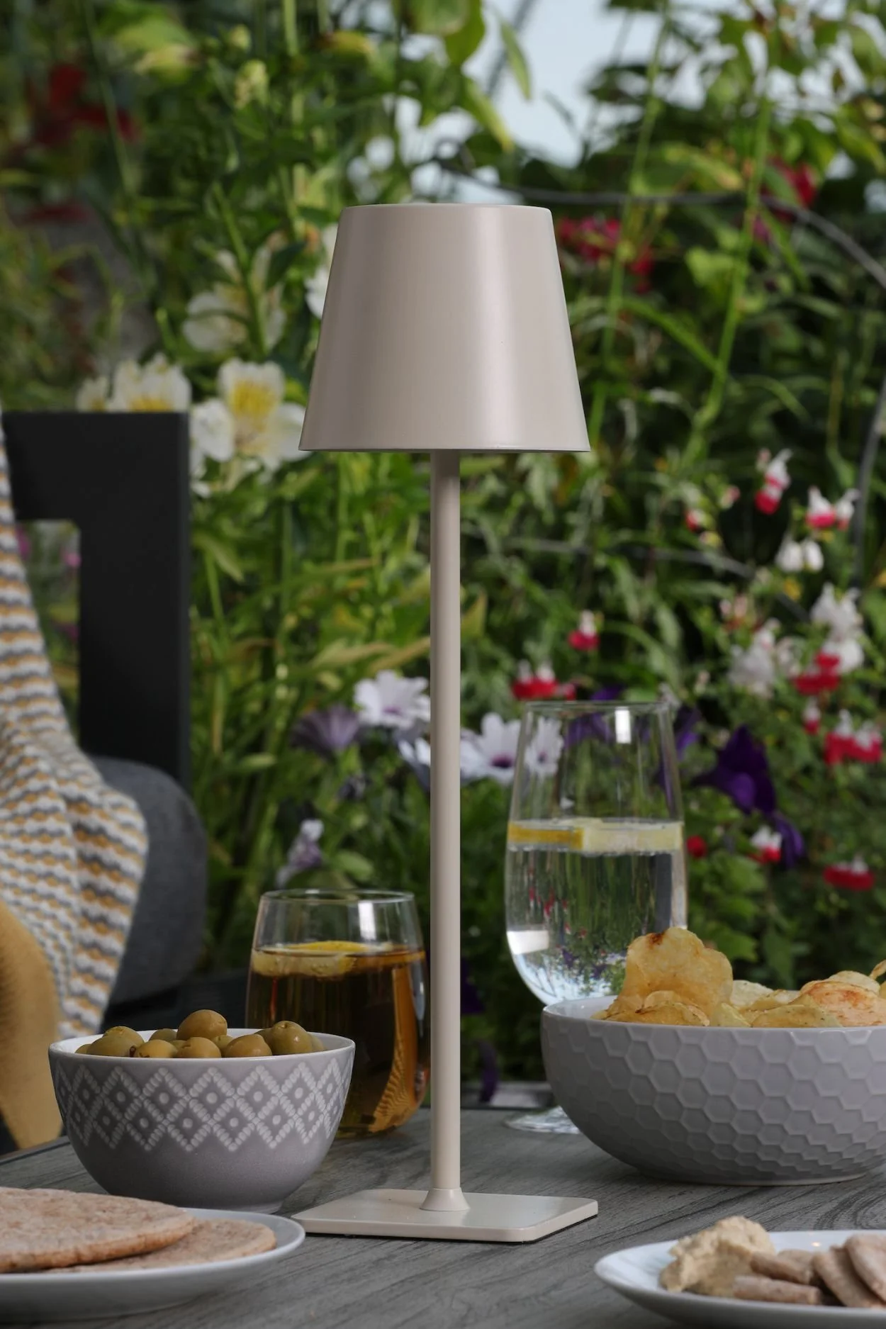 An outdoor lamp in grey metal on a wooden table with bowls of snacks
