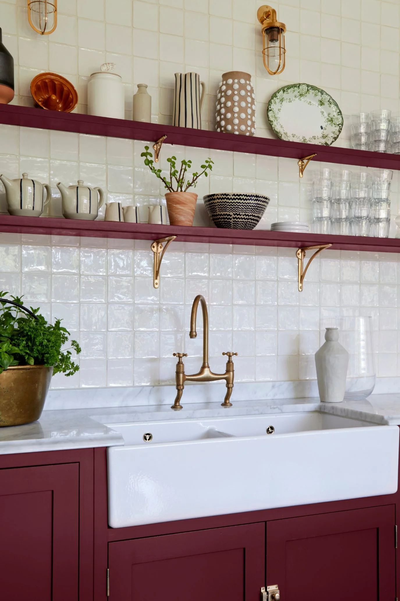A kitchen with cabinetry and slim shelves in a Bordeaux tone styled with ceramics, glasses, plants and other pieces of home decor