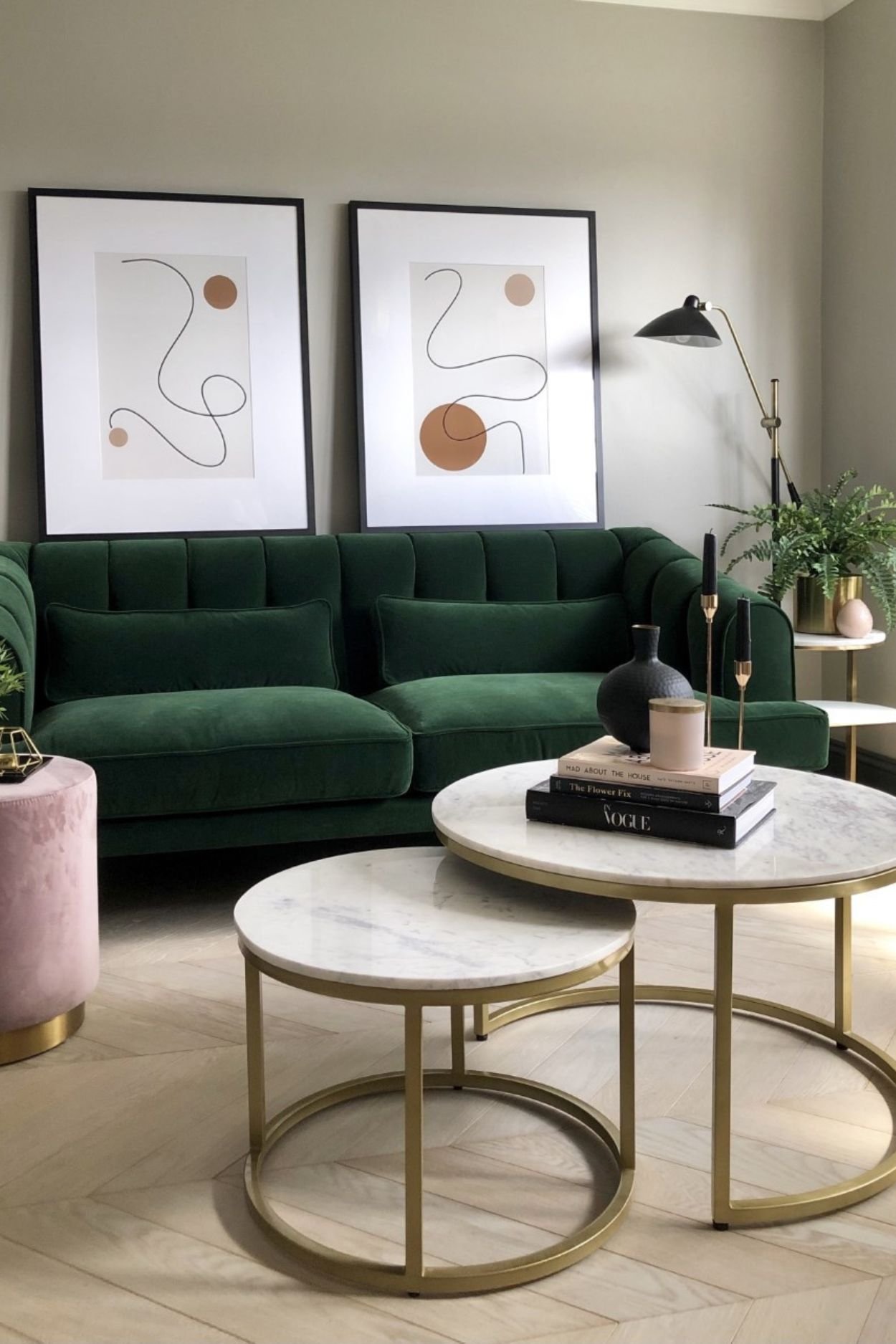 A green sofa with two nesting tables with books, vases and candle holders on top. Two large framed artwork are leaning against the sofa