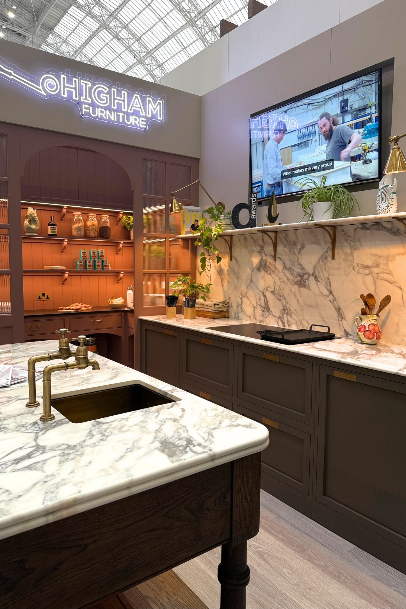Dark kitchen cabinetry with pale stone worktops and an illuminated open pantry displaying jars and kitchen accessories.