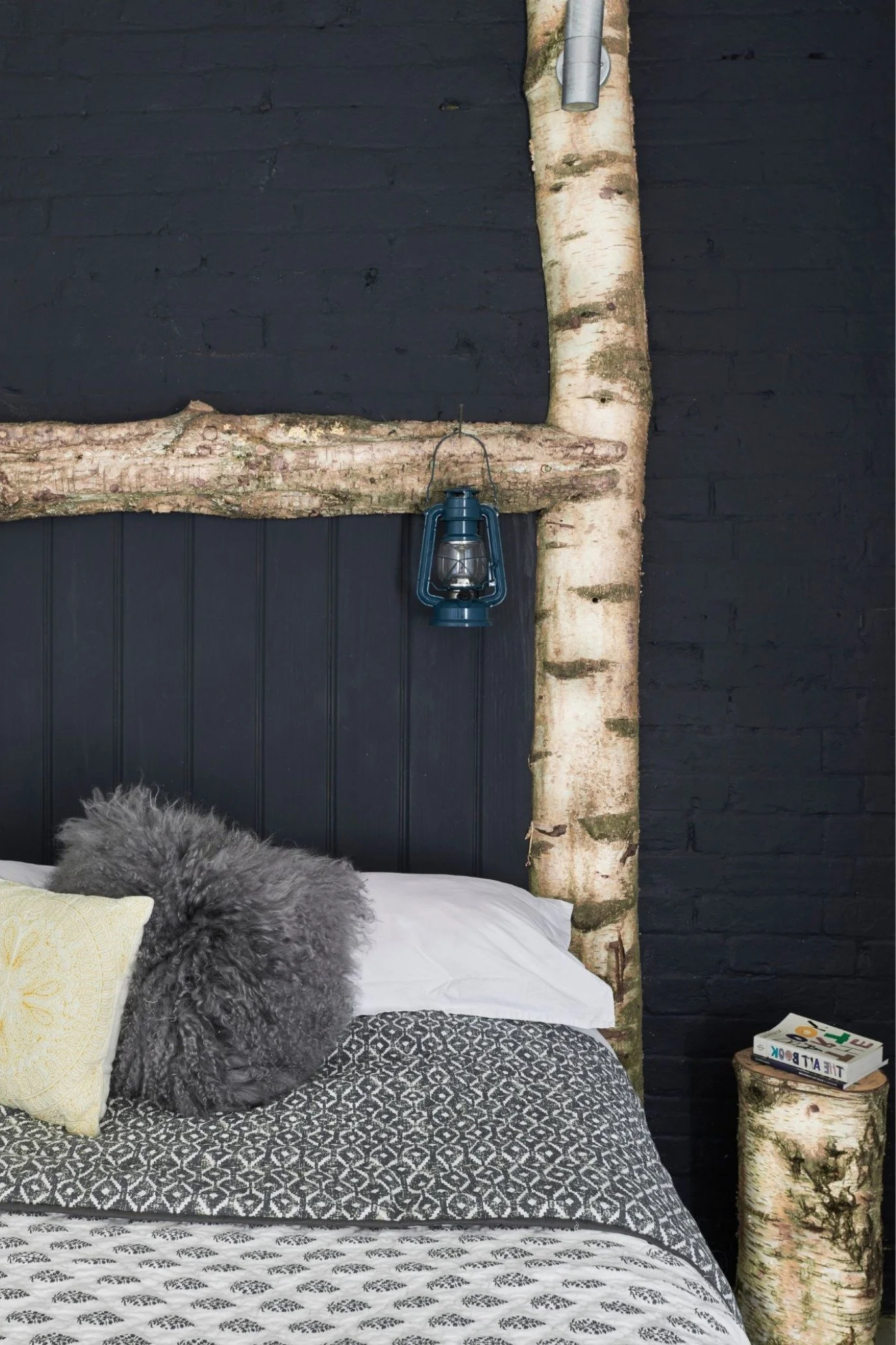 Unique handcrafted silver birch bed with layered bedding, black brick wall and rustic styling details.