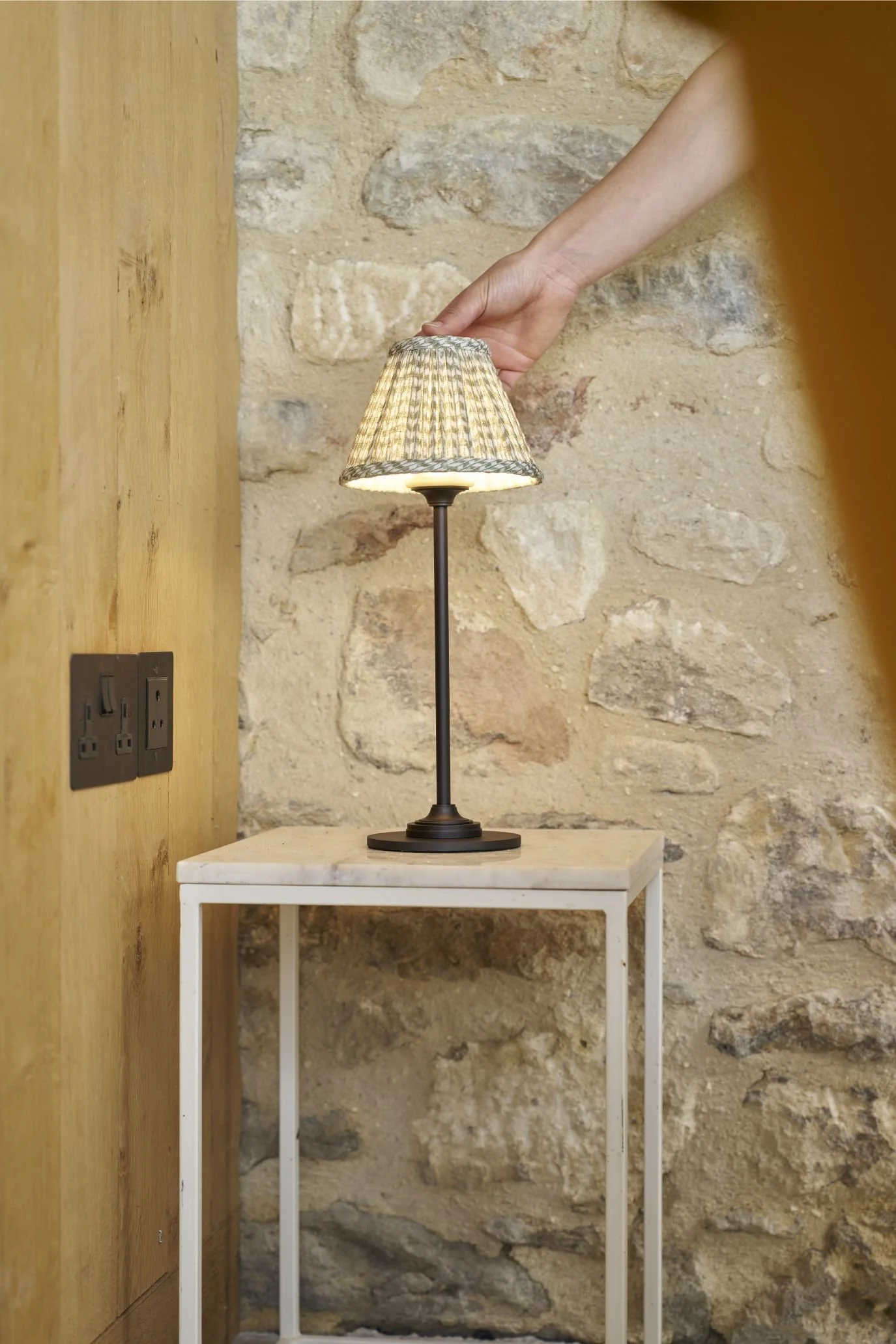 Small rechargeable table lamp on a side table against a textured stone wall