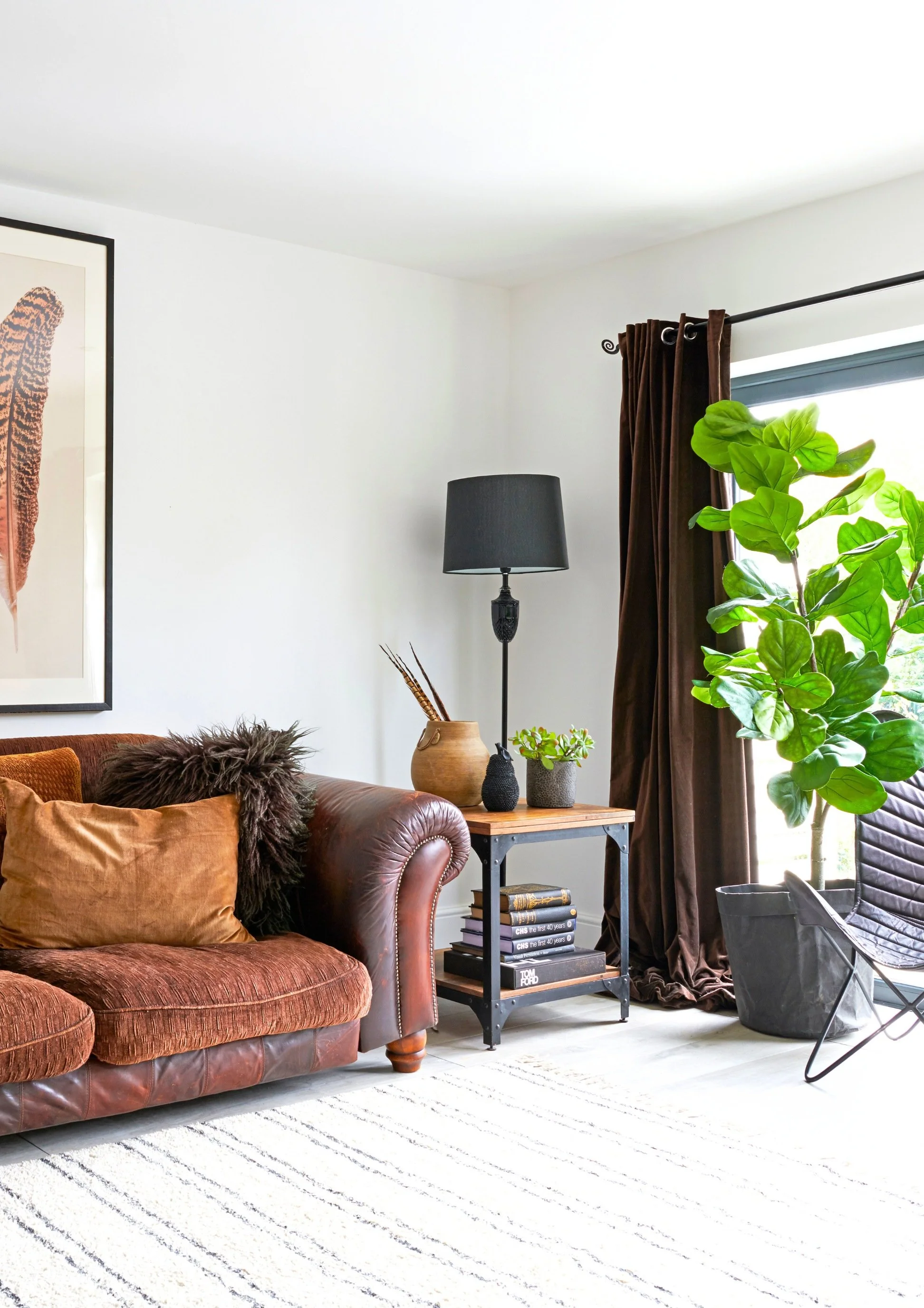 A room with a brown sofa, brown curtains and a side table with a tall black lamp