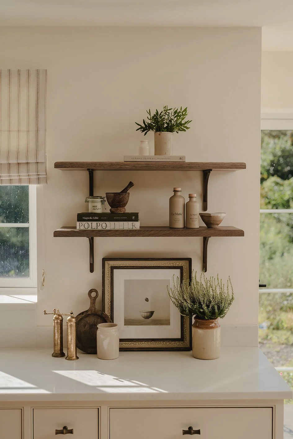 Two rustic wood shelves with aged brass brackets and books, plants and a pestle and mortar on the shelves