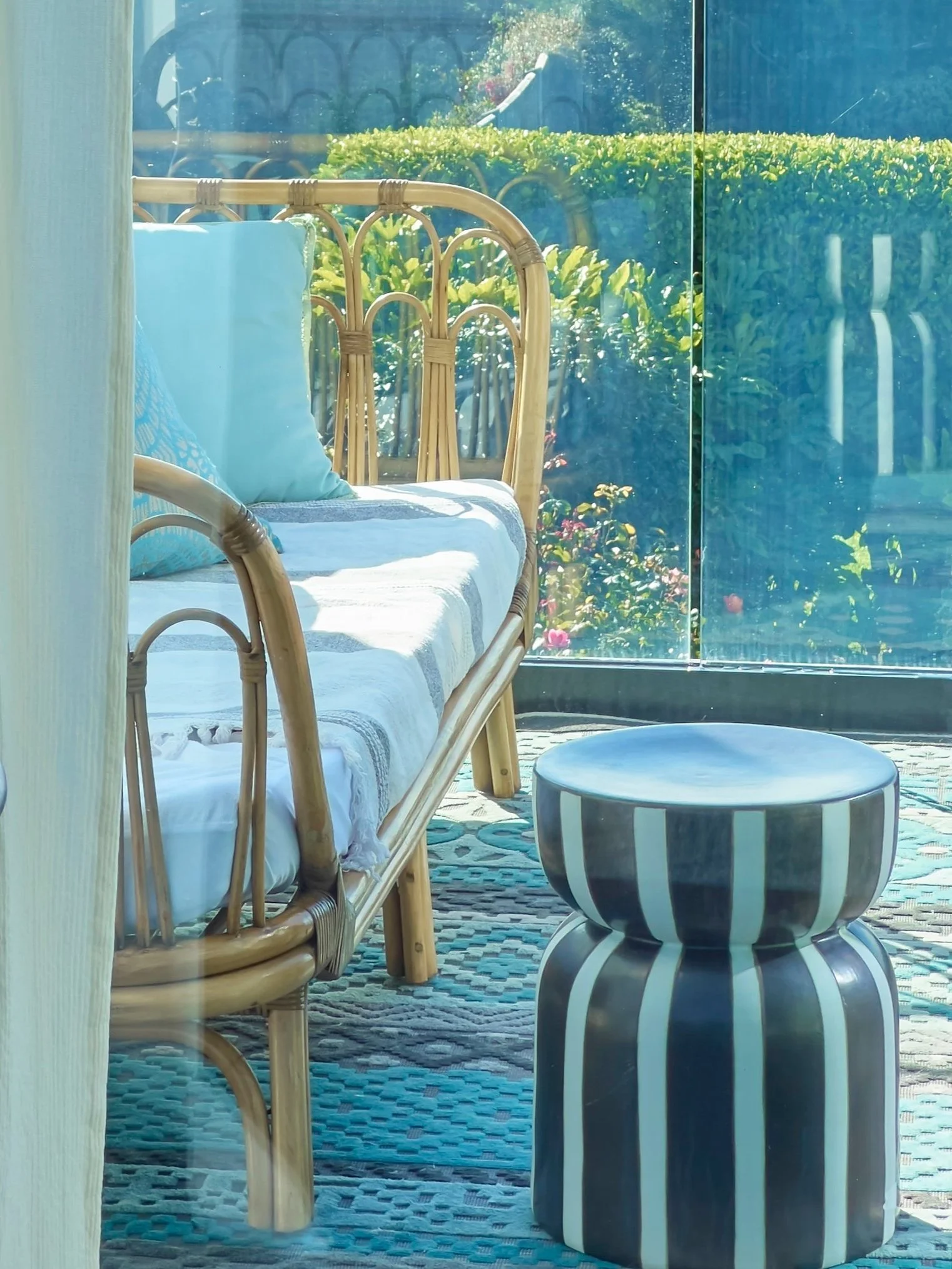 an outdoor rug on a balcony underneath a bamboo day bad with a black and white stripe ceramic table.