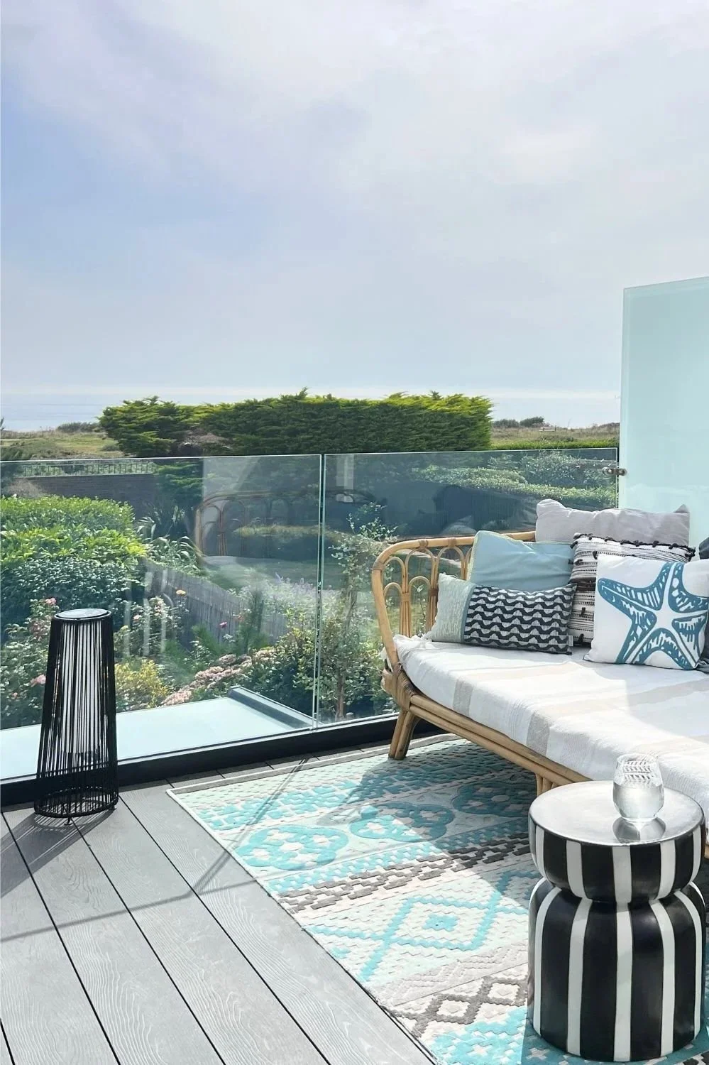 An aqua-toned patterned rug on a black decked balcony next to a bamboo bench with aqua cushions