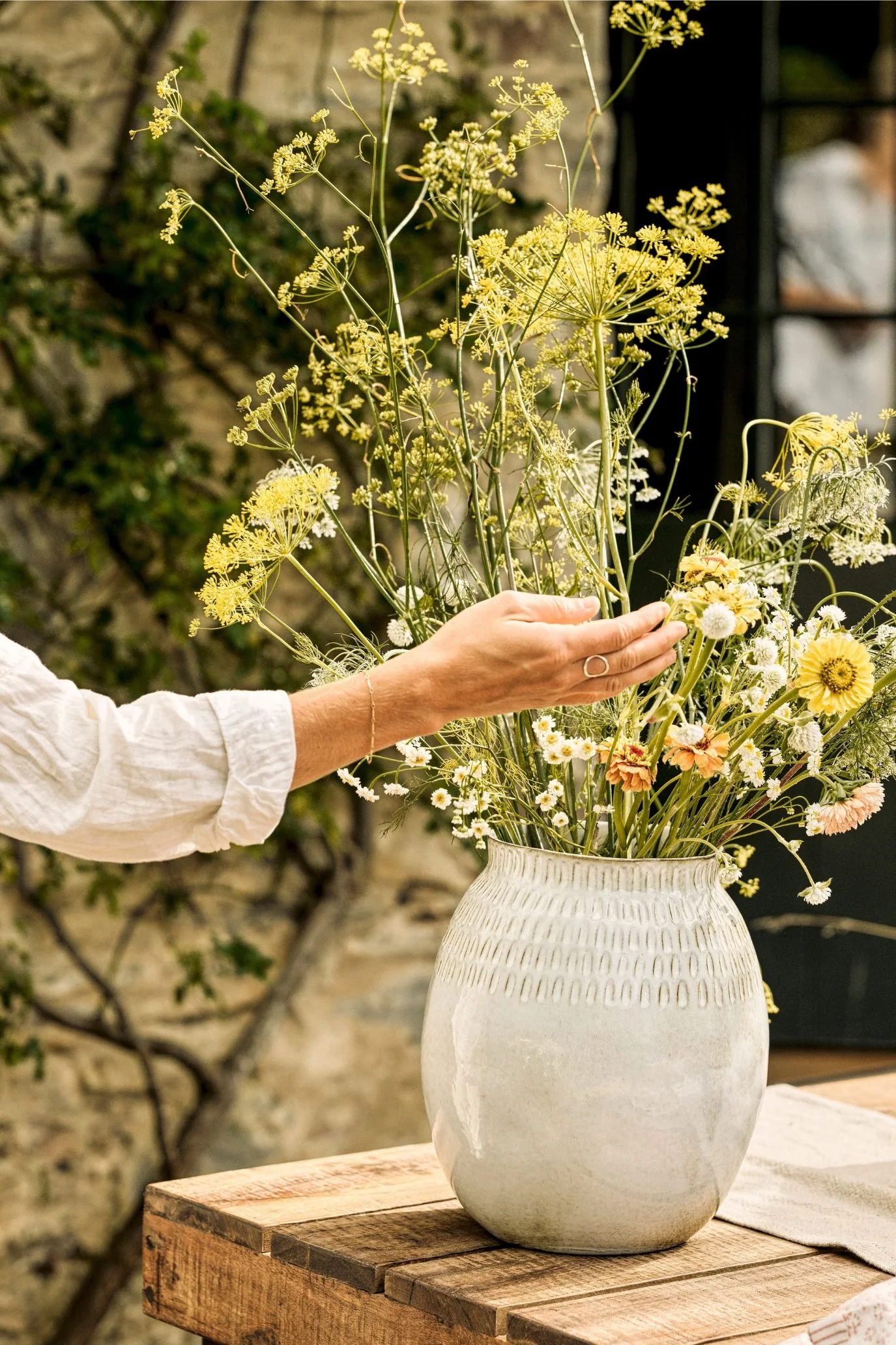 White glazed ceramic modern vase filled with fresh wildflowers on a wooden table.