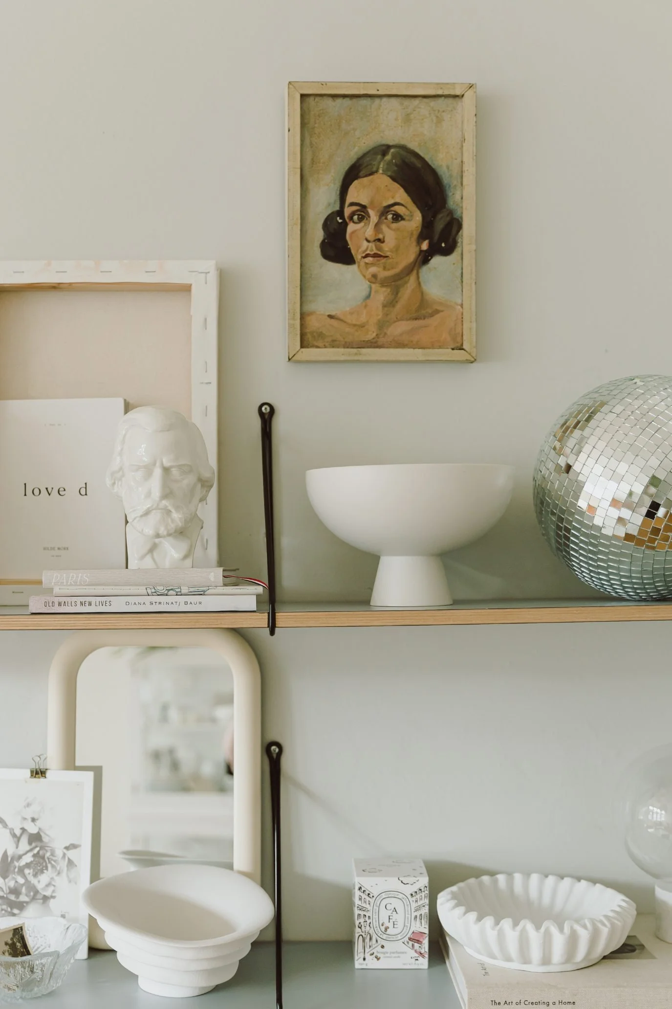Shelving styled with white home decor, frames  and a painting of a woman on the wall